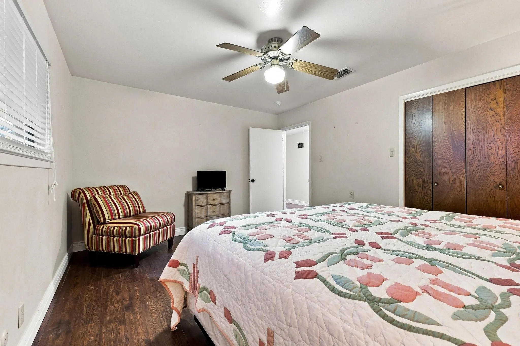 Wood-finish flooring, ceiling fan with integrated lighting, window with blinds, and built-in closet with wood doors