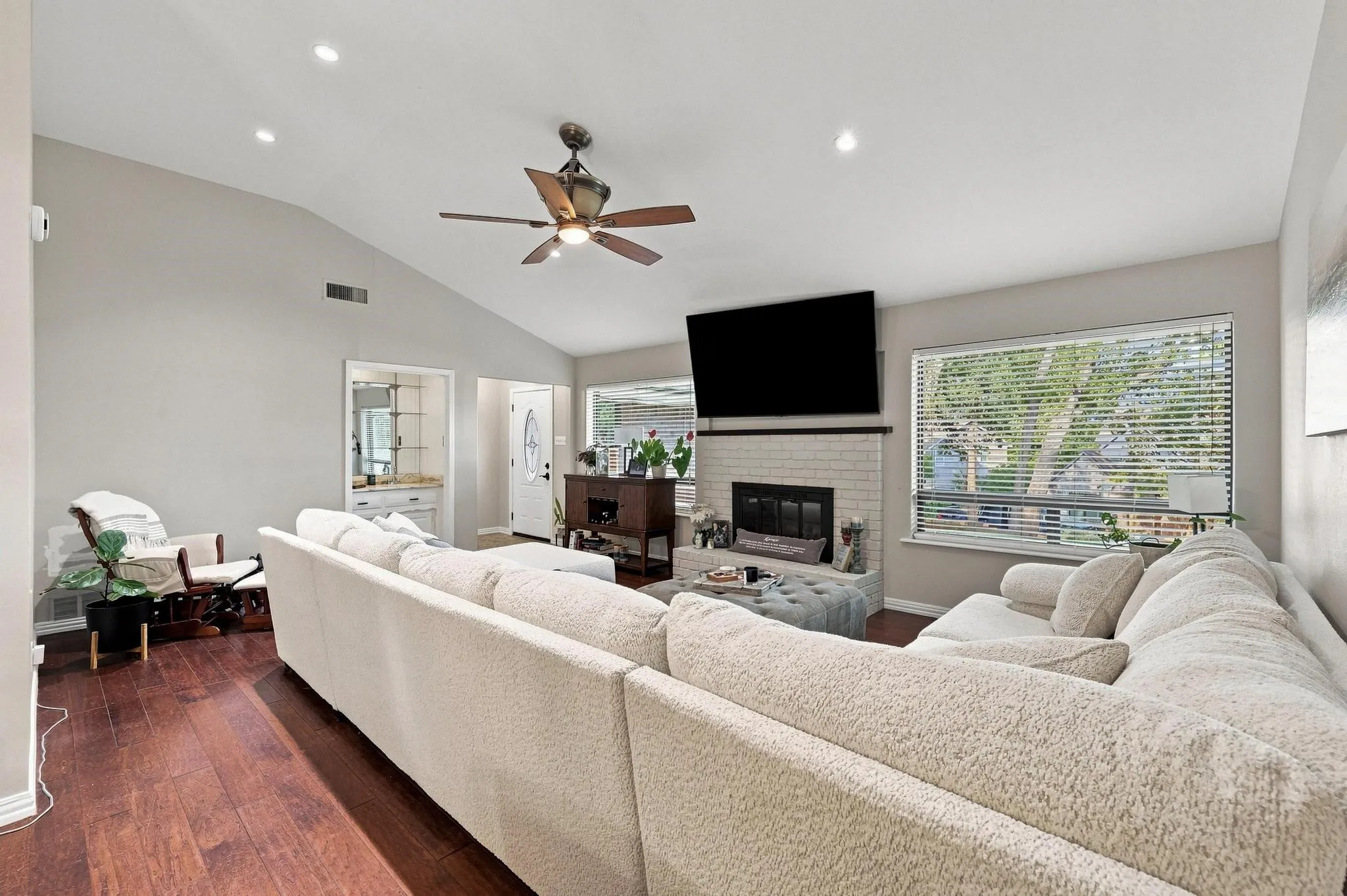 Spacious living area featuring wood-finish flooring, vaulted ceiling with recessed lighting, and a ceiling fan