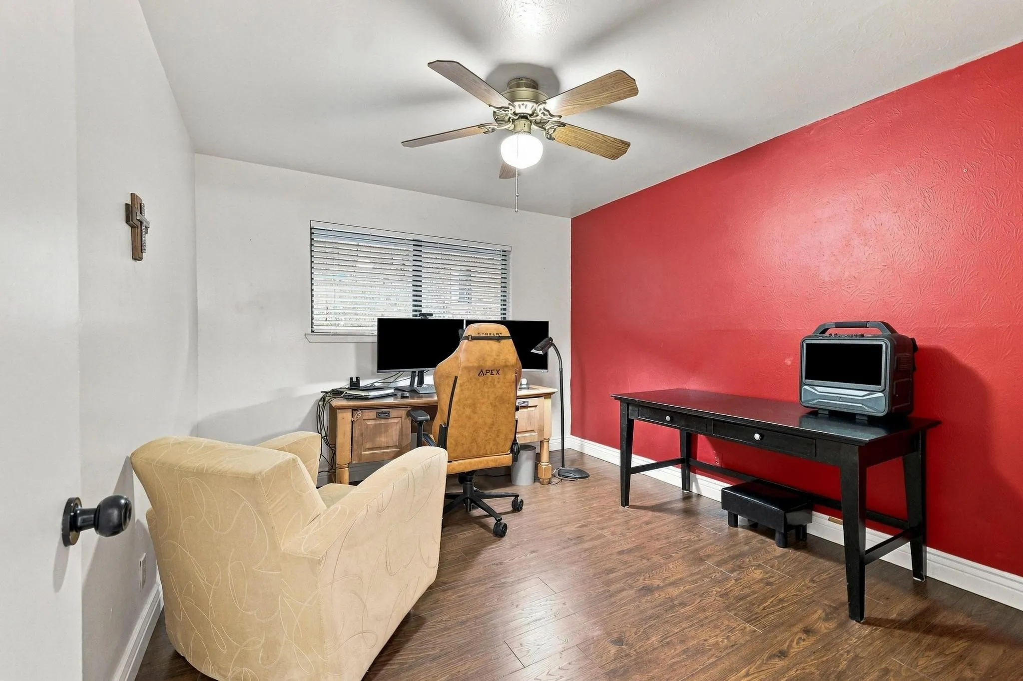Wood-finish flooring, ceiling fan with integrated lighting, window with blinds, and contrasting accent wall