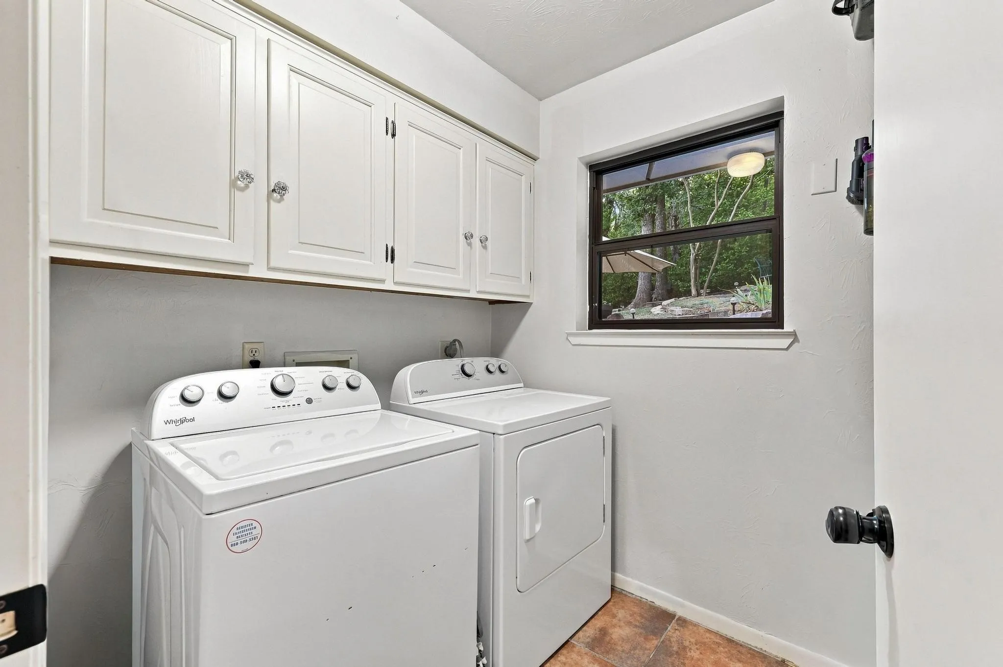 White upper cabinetry with clear knob hardware, a dark-framed window, and tile flooring