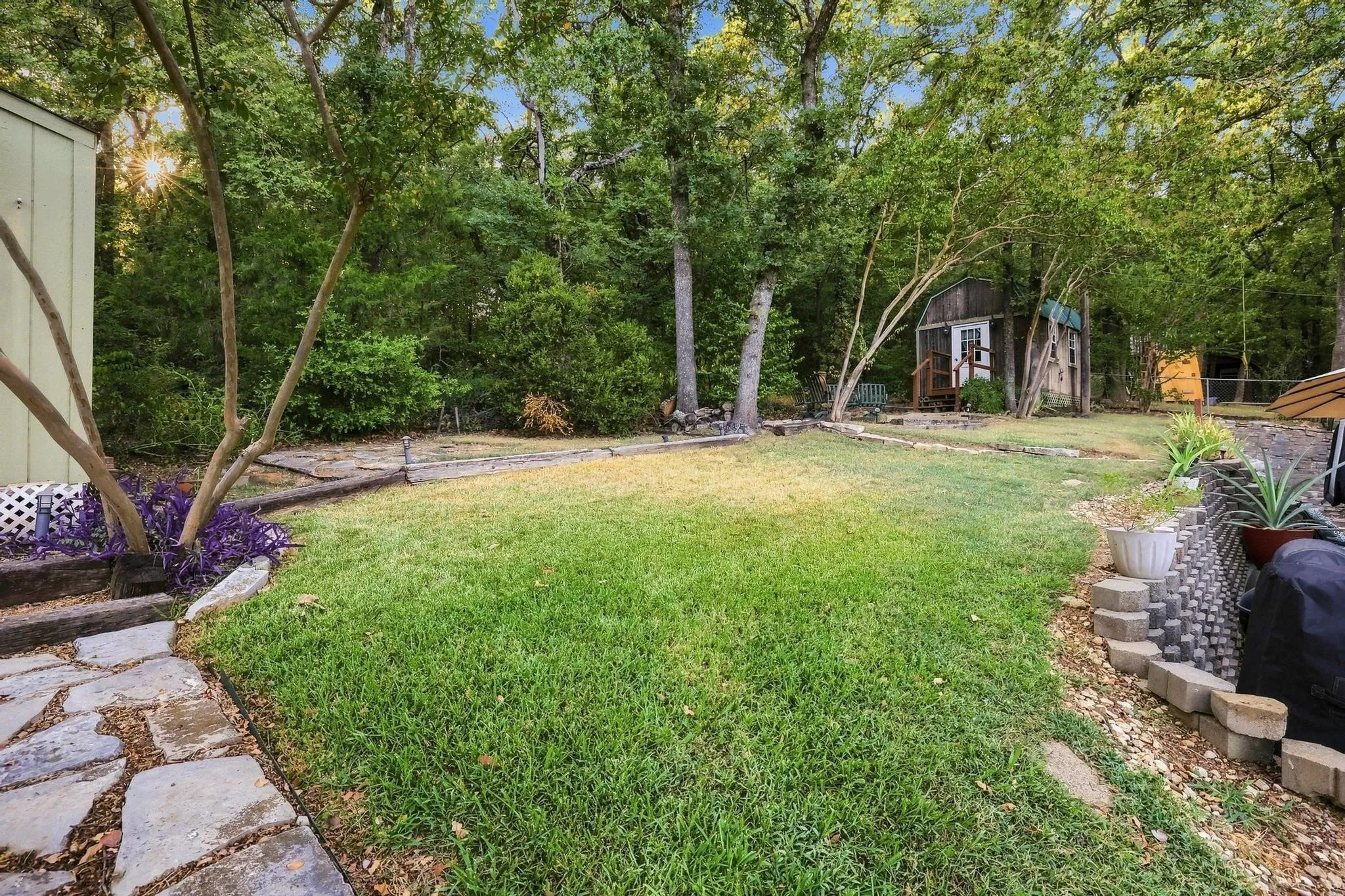 Expansive backyard featuring a stone pathway, manicured lawn, and mature trees, with a detached shed structure