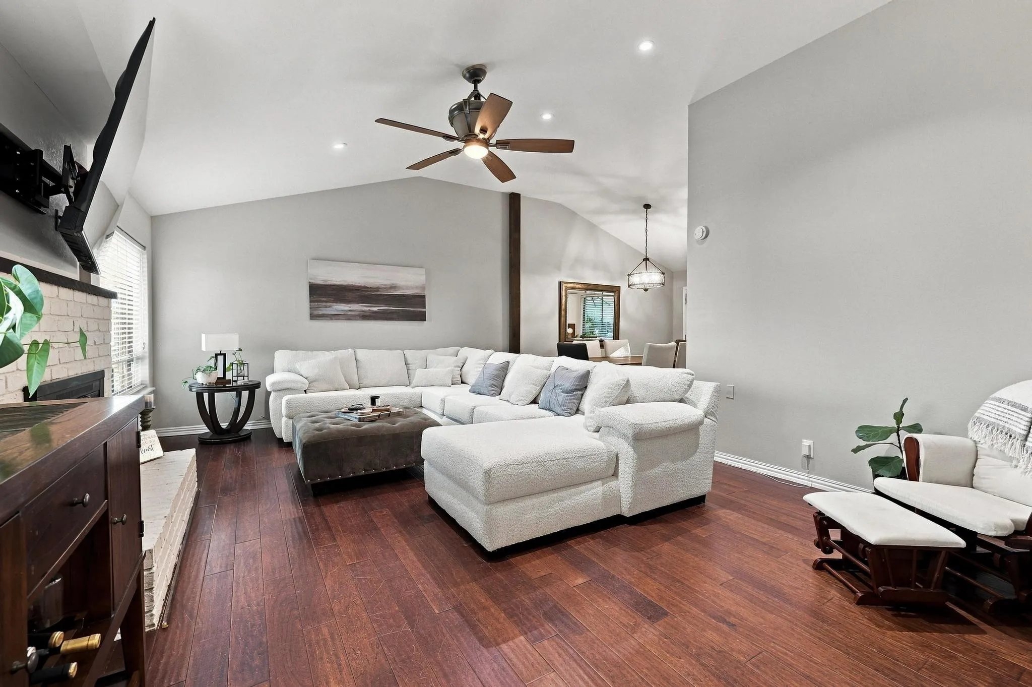 Vaulted ceilings, wood-finish flooring, recessed lighting, ceiling fan, and a painted brick fireplace