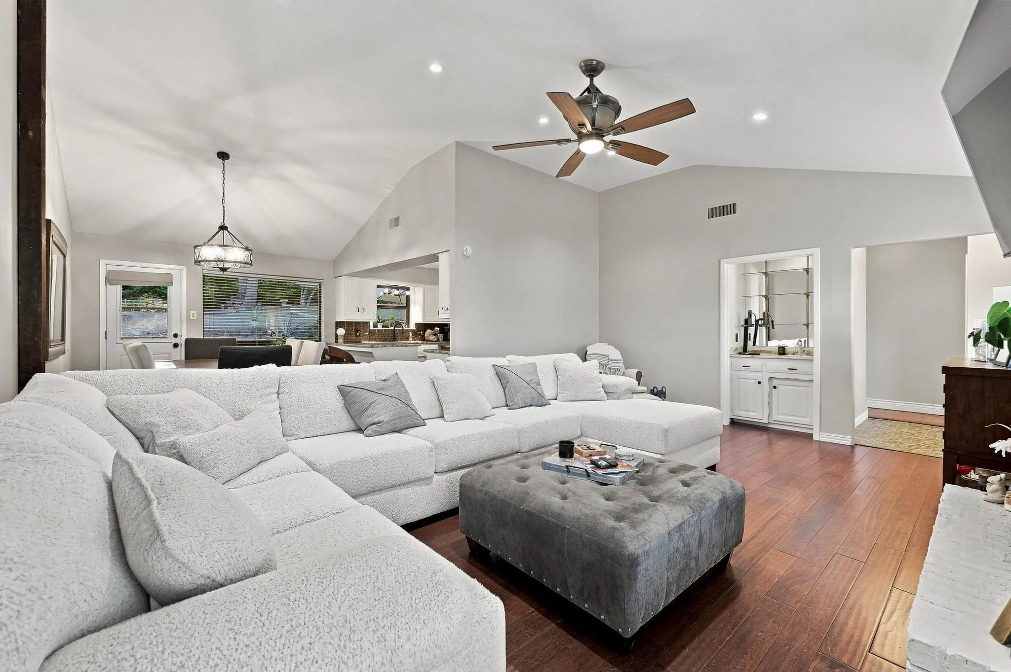 Vaulted ceilings, wood-finish flooring, recessed lighting, built-in wet bar with mirrored shelving, and a decorative ceiling fan