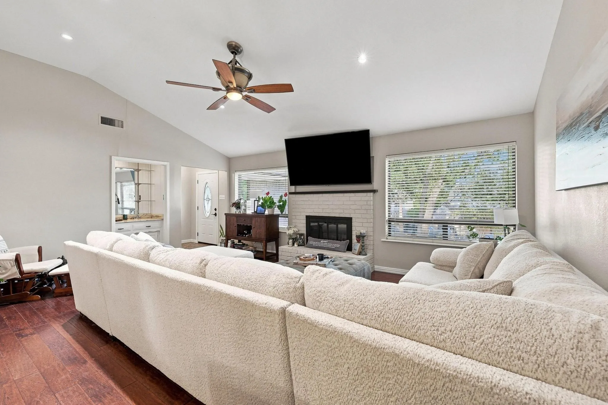 Vaulted ceiling with a ceiling fan, recessed lighting, wood-finish flooring, a white brick fireplace, and a built-in wet bar