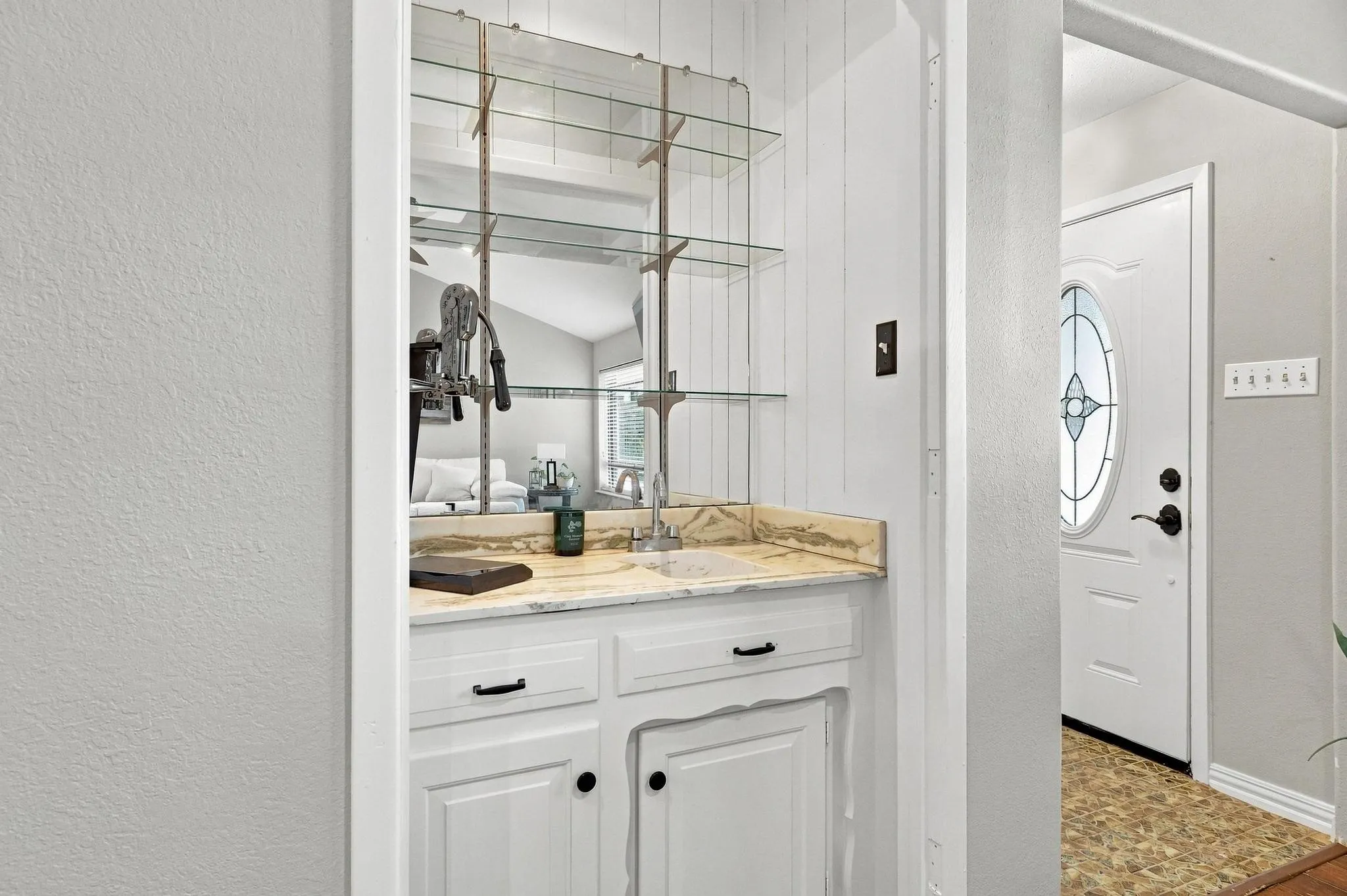 Built-in wet bar featuring a mirrored backsplash, glass shelving, and a light-toned countertop