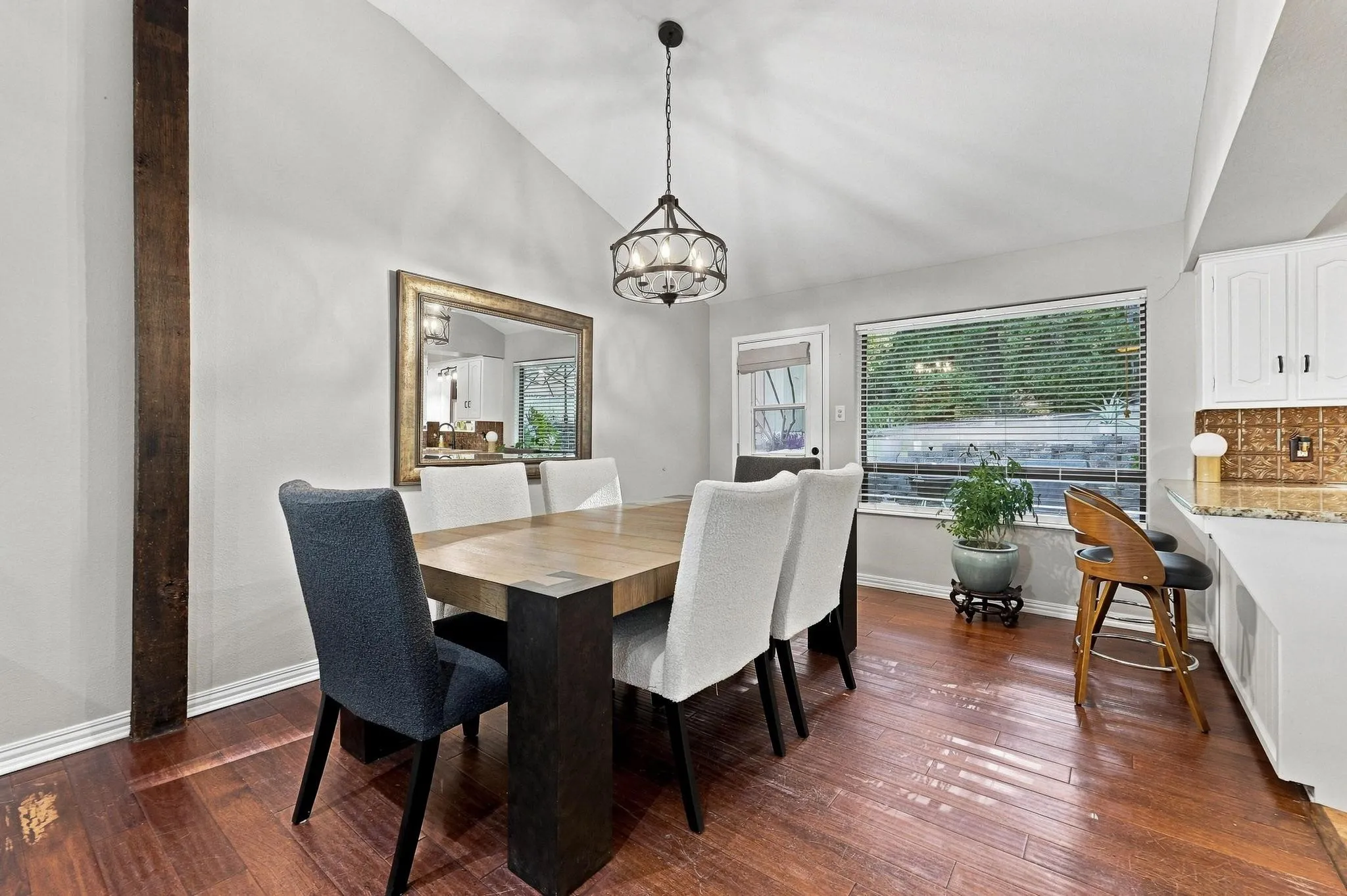 Vaulted ceiling with an ornamental chandelier, wood-finish flooring, and built-in white cabinetry with a tile backsplash