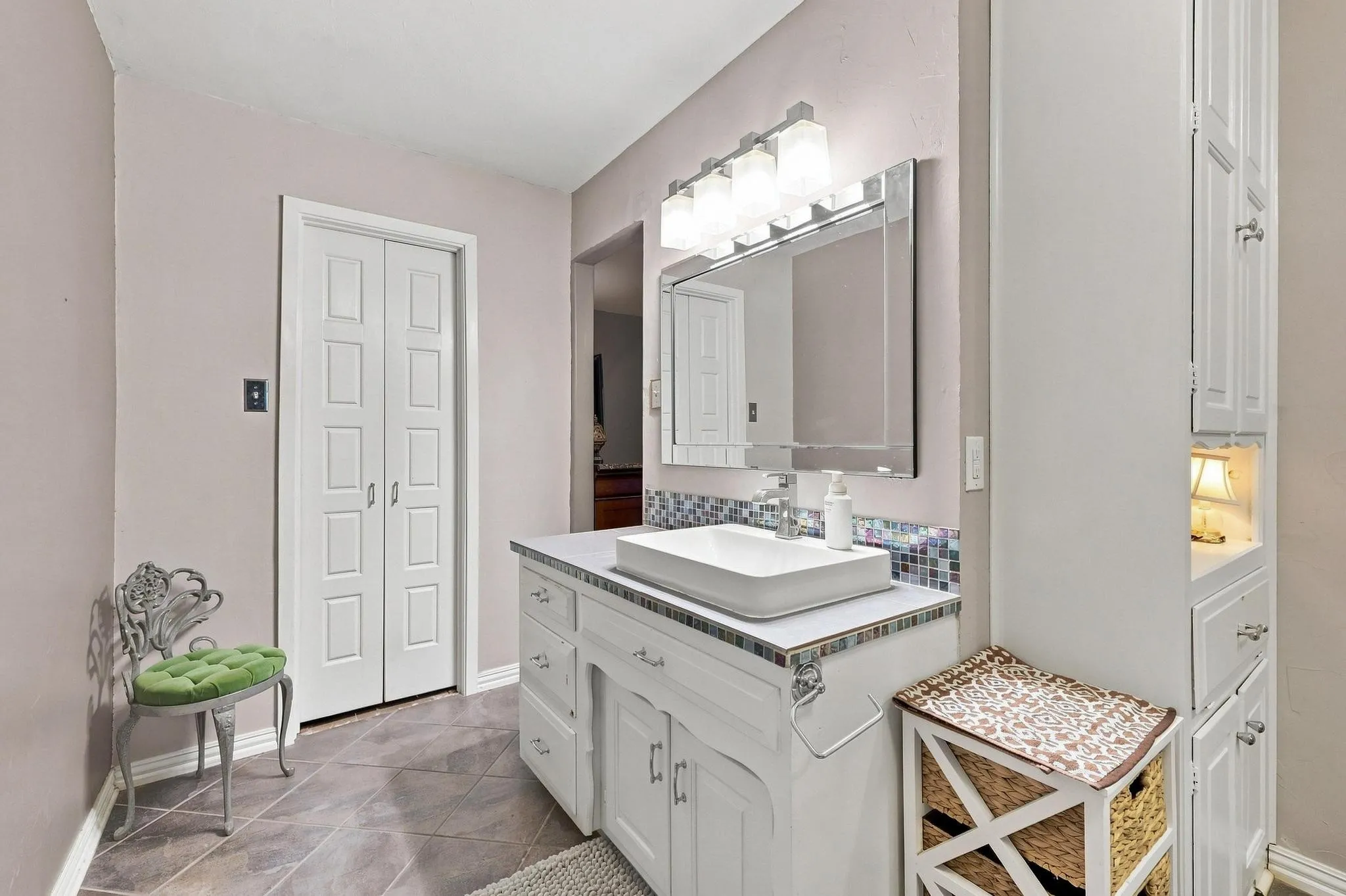 White vanity with a vessel sink, mosaic tile backsplash, and a large framed mirror