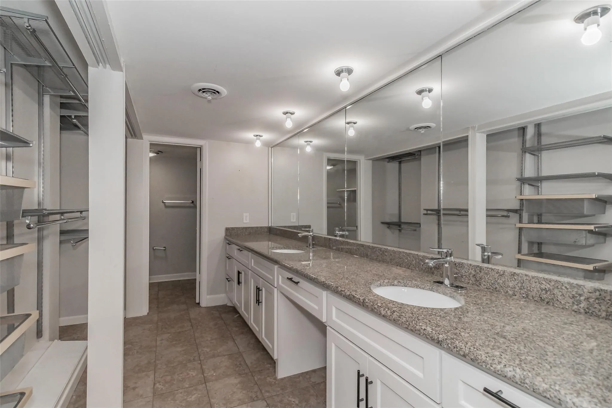 Expansive dual vanity with a patterned countertop, dual undermount sinks, and white cabinetry with dark hardware