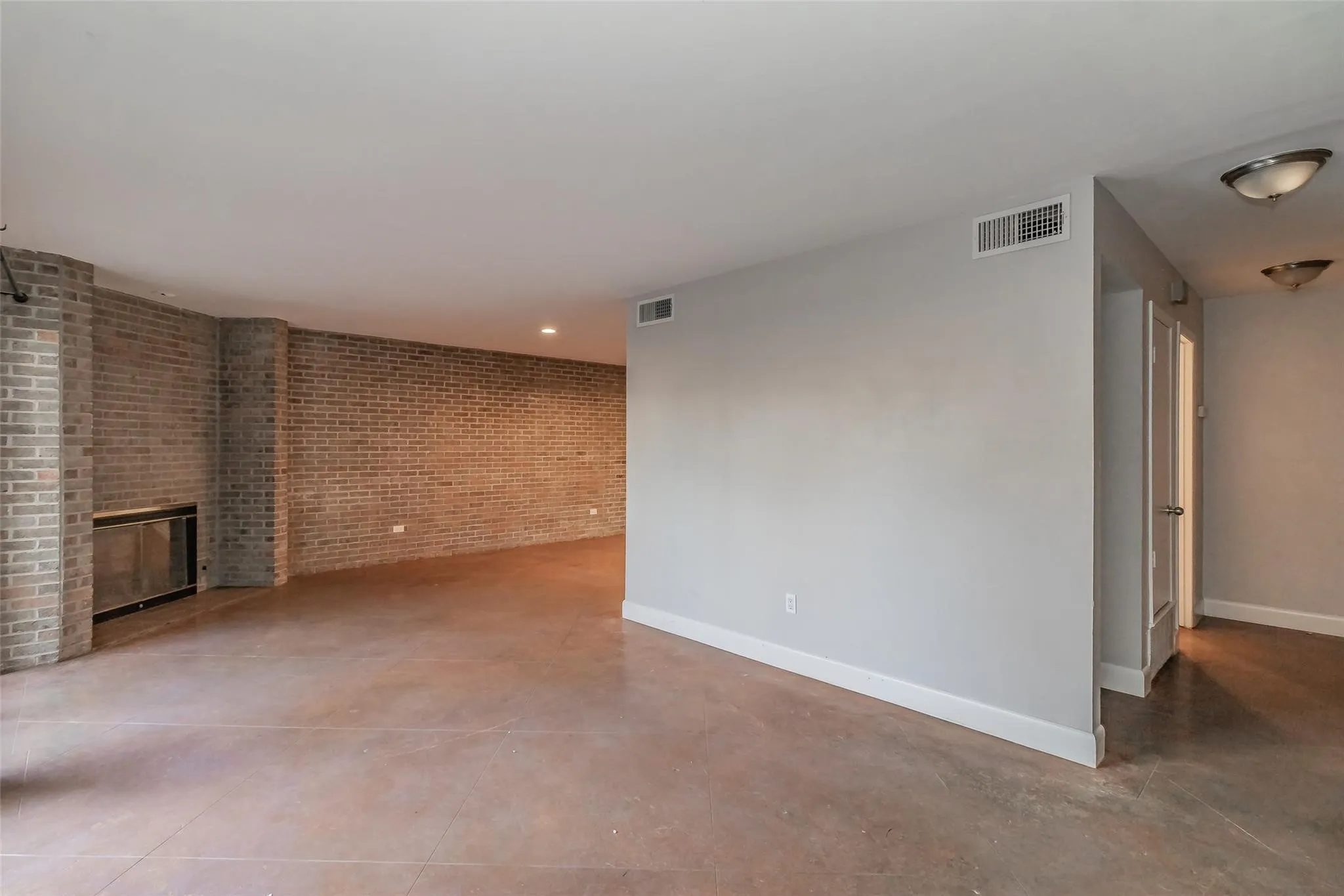 Exposed brick wall, recessed lighting, fireplace with a glass enclosure, light gray painted walls, and concrete-finish flooring