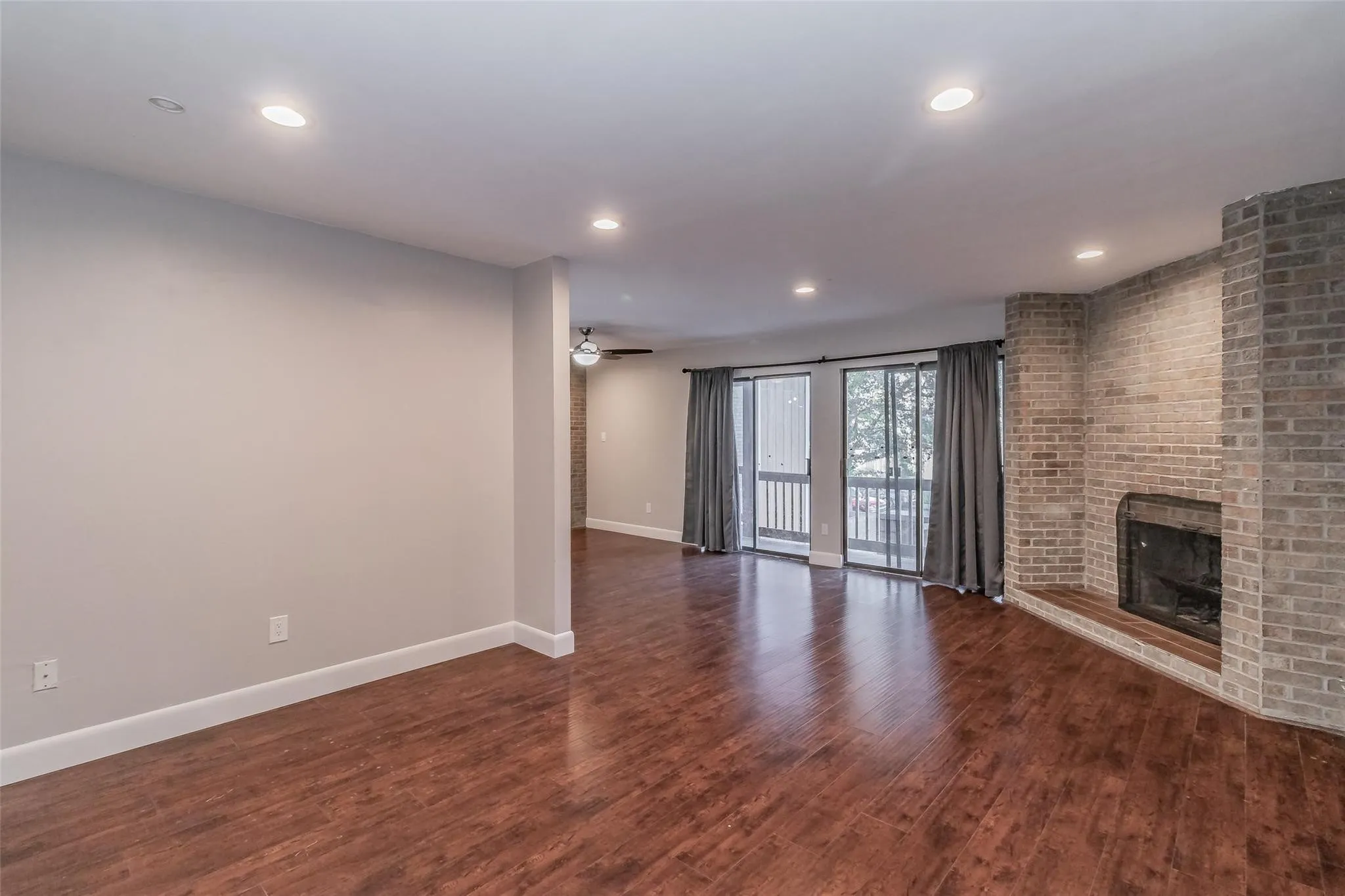 Hardwood-finish flooring throughout, recessed lighting, brick fireplace with hearth, and sliding glass doors with balcony access