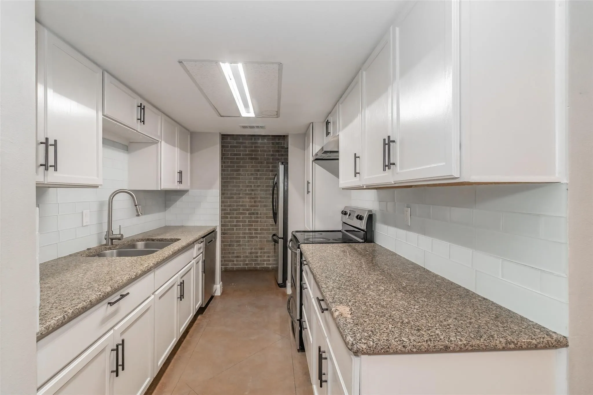 Galley kitchen featuring white cabinetry with dark hardware, stone-finish countertops, subway tile backsplash, and stainless steel appliances