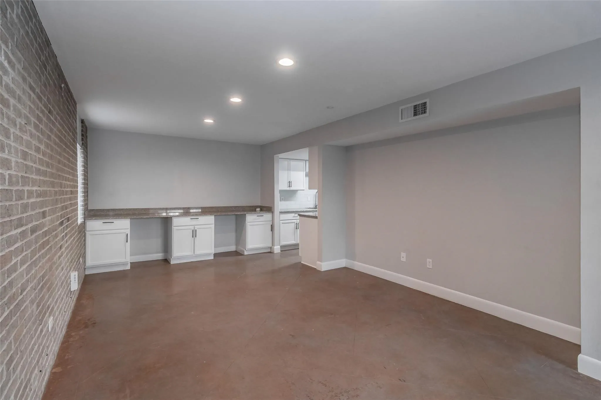Exposed brick accent wall, recessed lighting, built-in cabinetry with stone countertops, concrete-finish flooring, and white baseboards