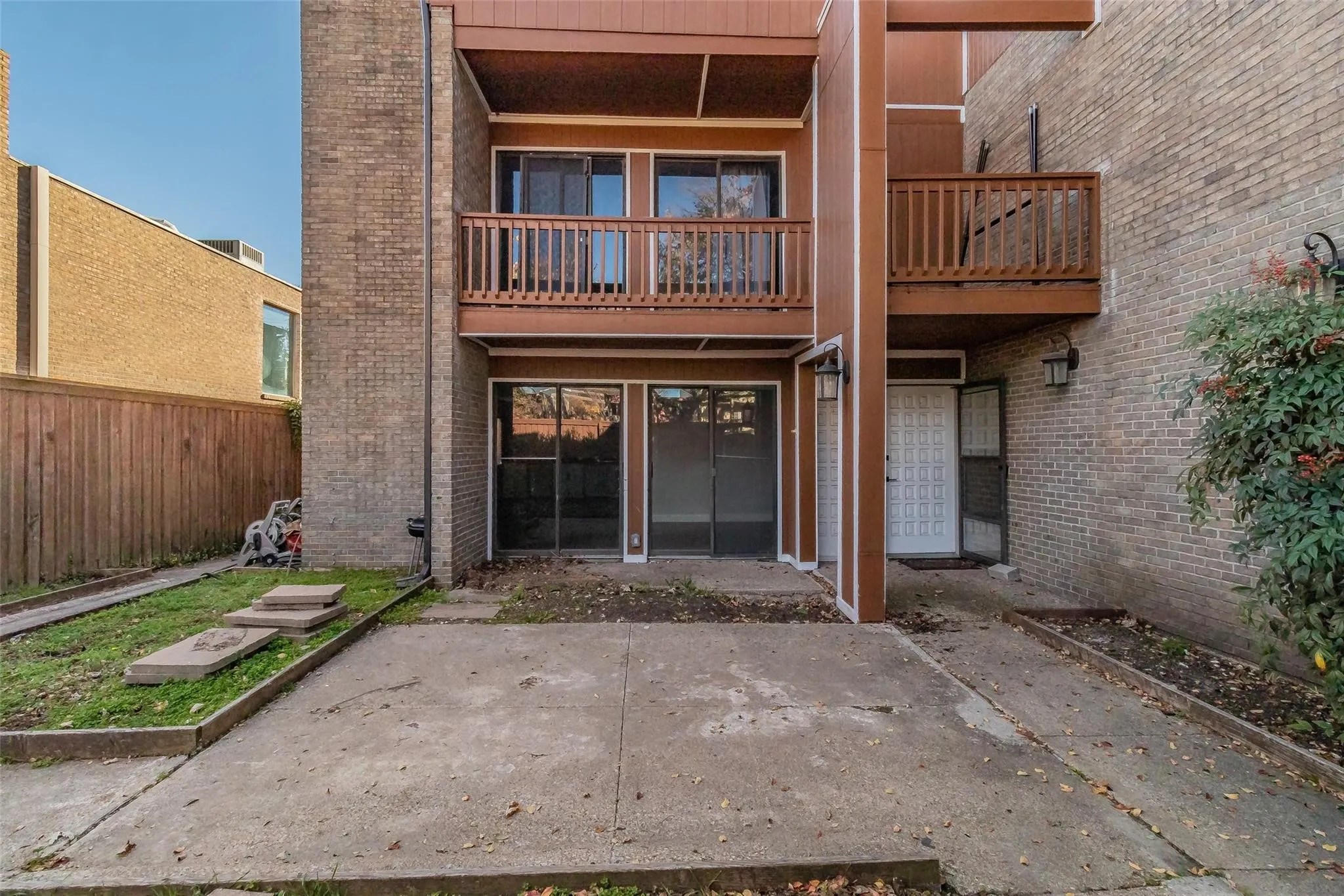 Brick exterior with wood-finish siding, ground-level patio, and an upper-level balcony