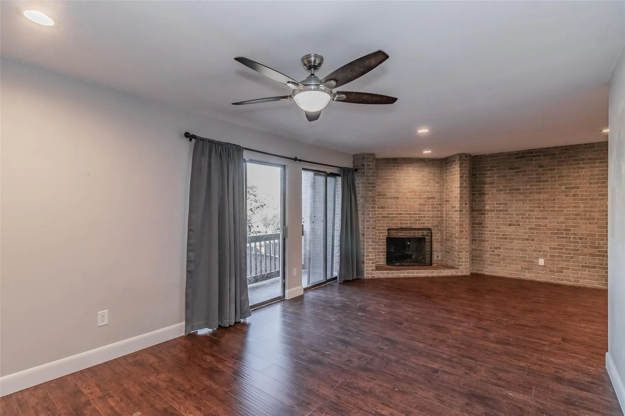 Wood-finish flooring, recessed lighting, ceiling fan, brick-faced fireplace, and sliding glass doors
