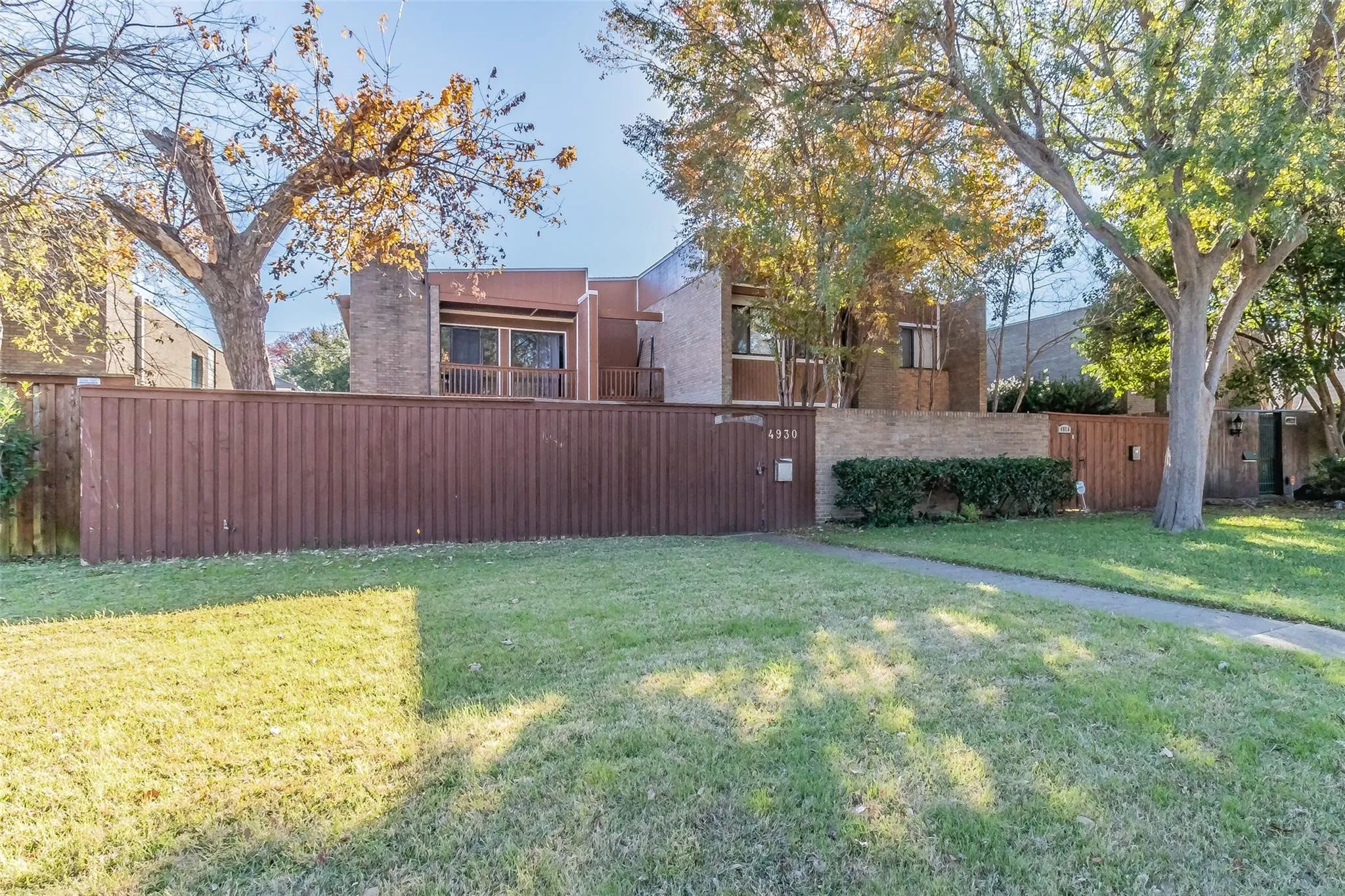 Brick-clad exterior with a private balcony, wood fence, and mature trees