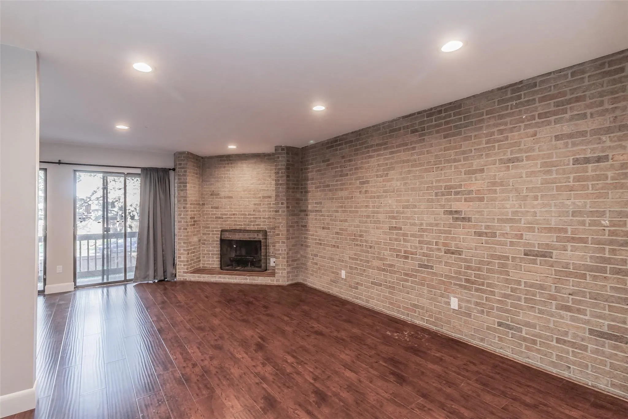 Wood-finish flooring, recessed lighting, brick accent wall, built-in fireplace, and sliding glass doors to outdoor space