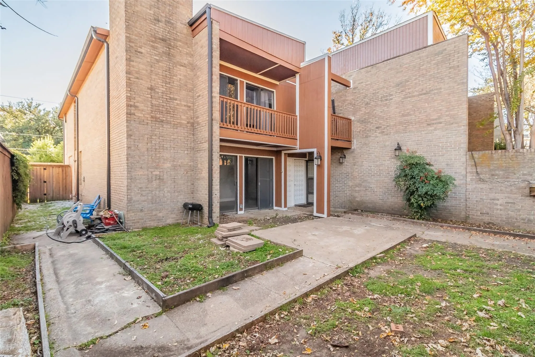 Brick exterior with a second-story wood-finish balcony, ground-level patio door, and concrete patio area