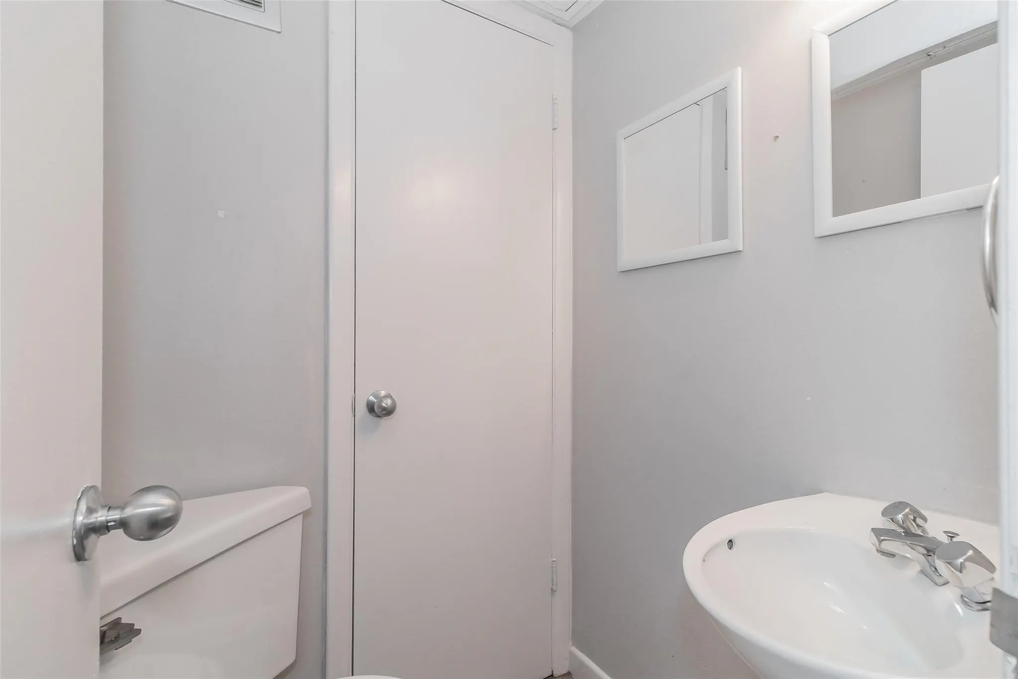 Pedestal sink with chrome faucet, wall-mounted mirror, and white interior door