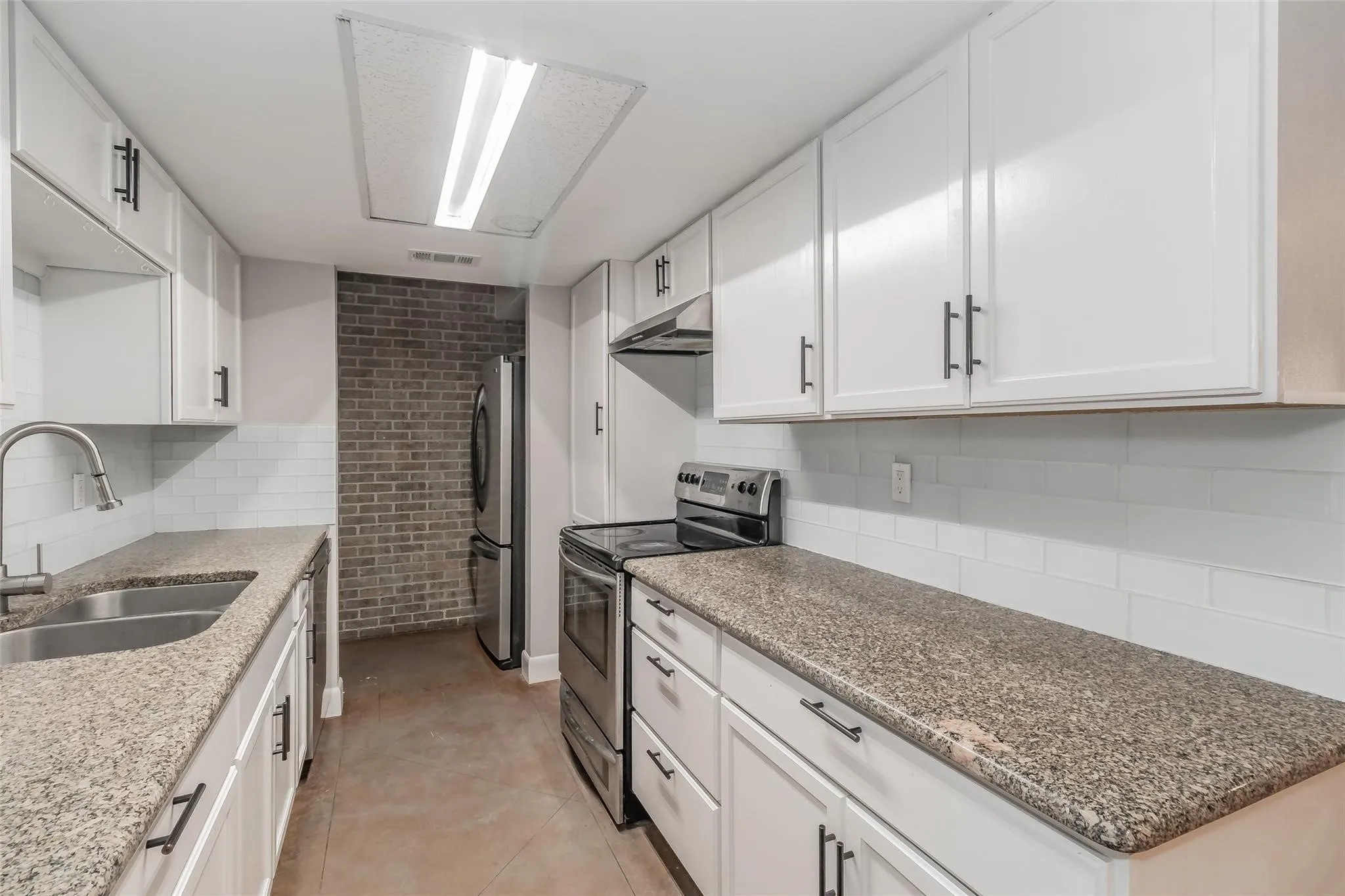 Kitchen featuring white cabinetry, granite countertops, a stainless steel double sink, and a subway tile backsplash