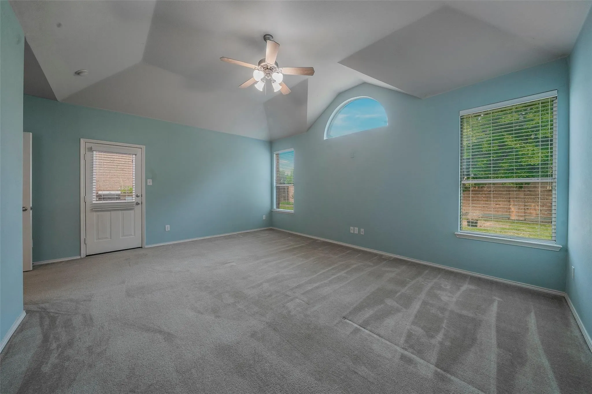 Carpeted spare room featuring vaulted ceiling and ceiling fan