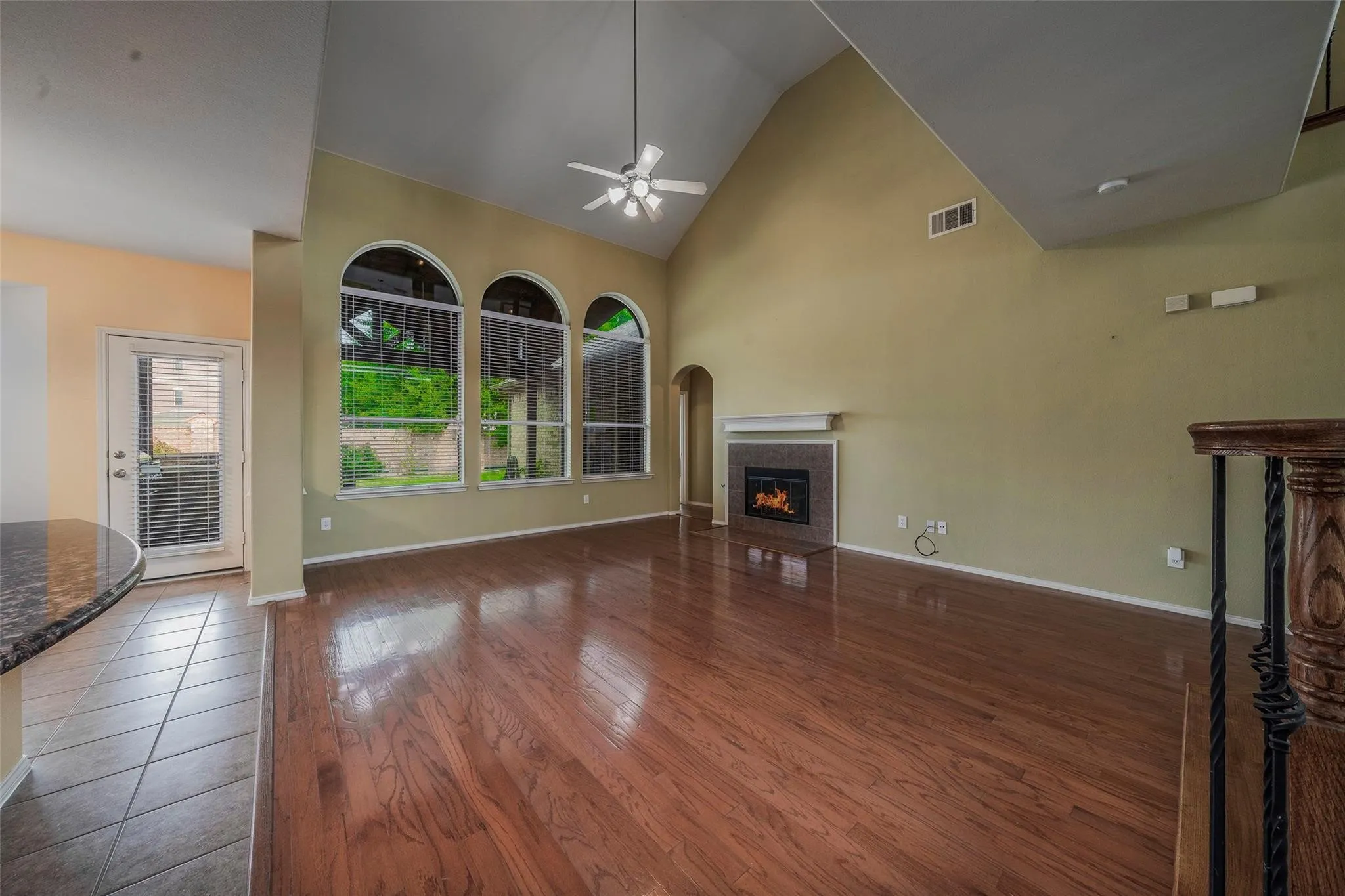 Unfurnished living room featuring ceiling fan, a tile fireplace, dark wood-type flooring, and high vaulted ceiling