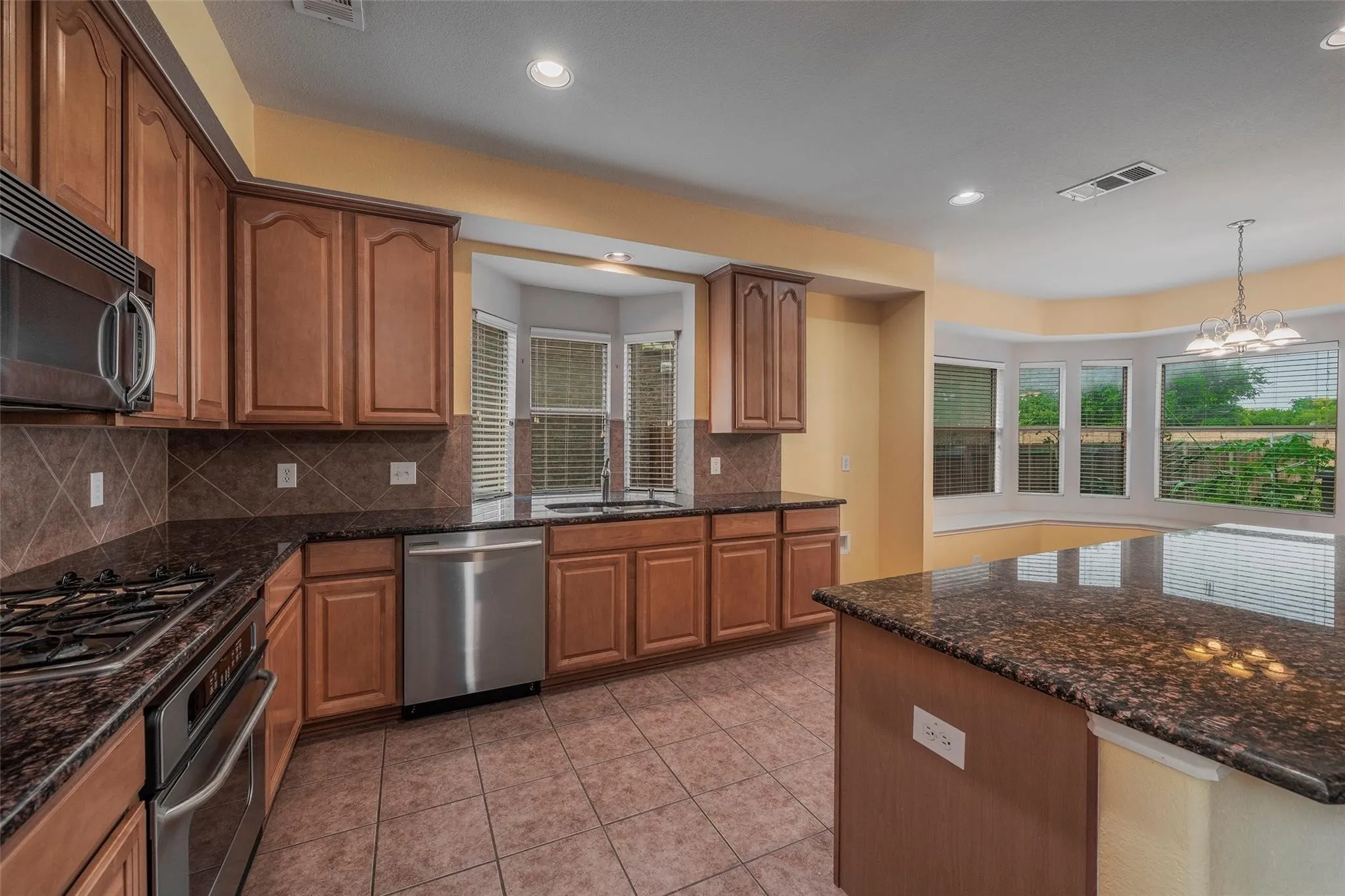 Kitchen featuring backsplash, stainless steel appliances, sink, pendant lighting, and an inviting chandelier