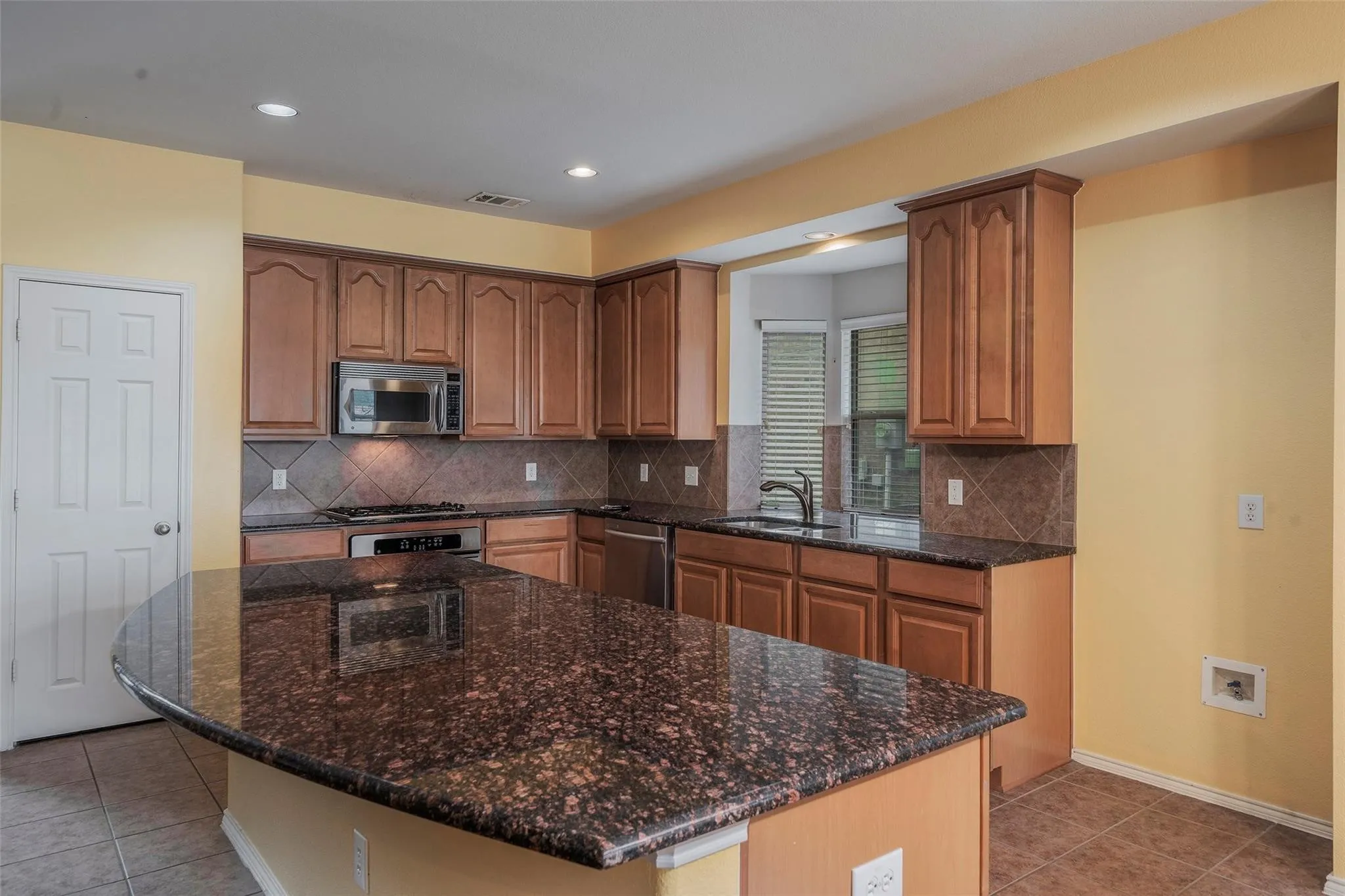 Kitchen with light tile patterned flooring, dark stone countertops, sink, and appliances with stainless steel finishes