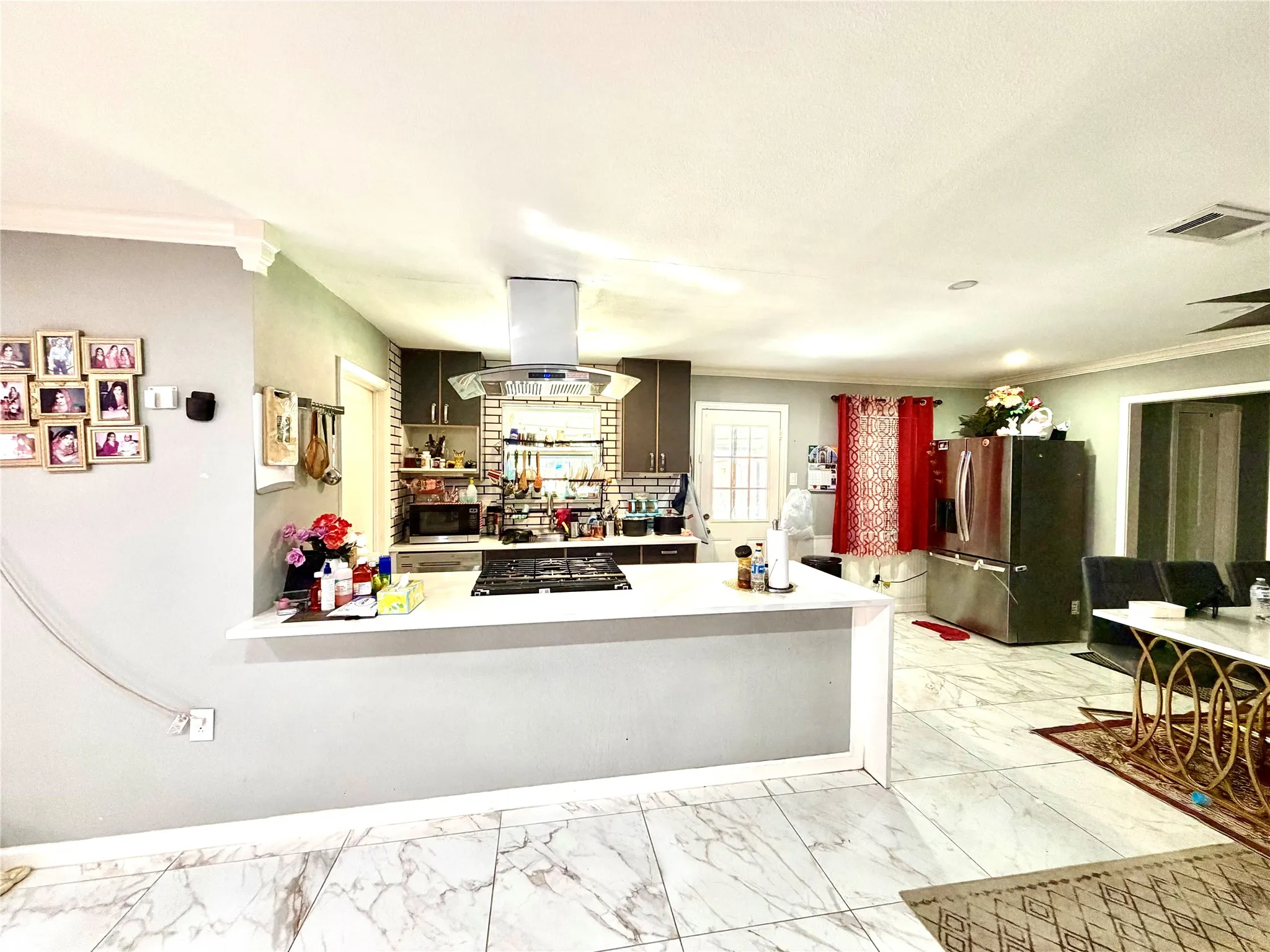 Open-concept kitchen featuring marble-look tile flooring, white countertop peninsula, dark wood-finish cabinetry, and a stainless steel island range hood