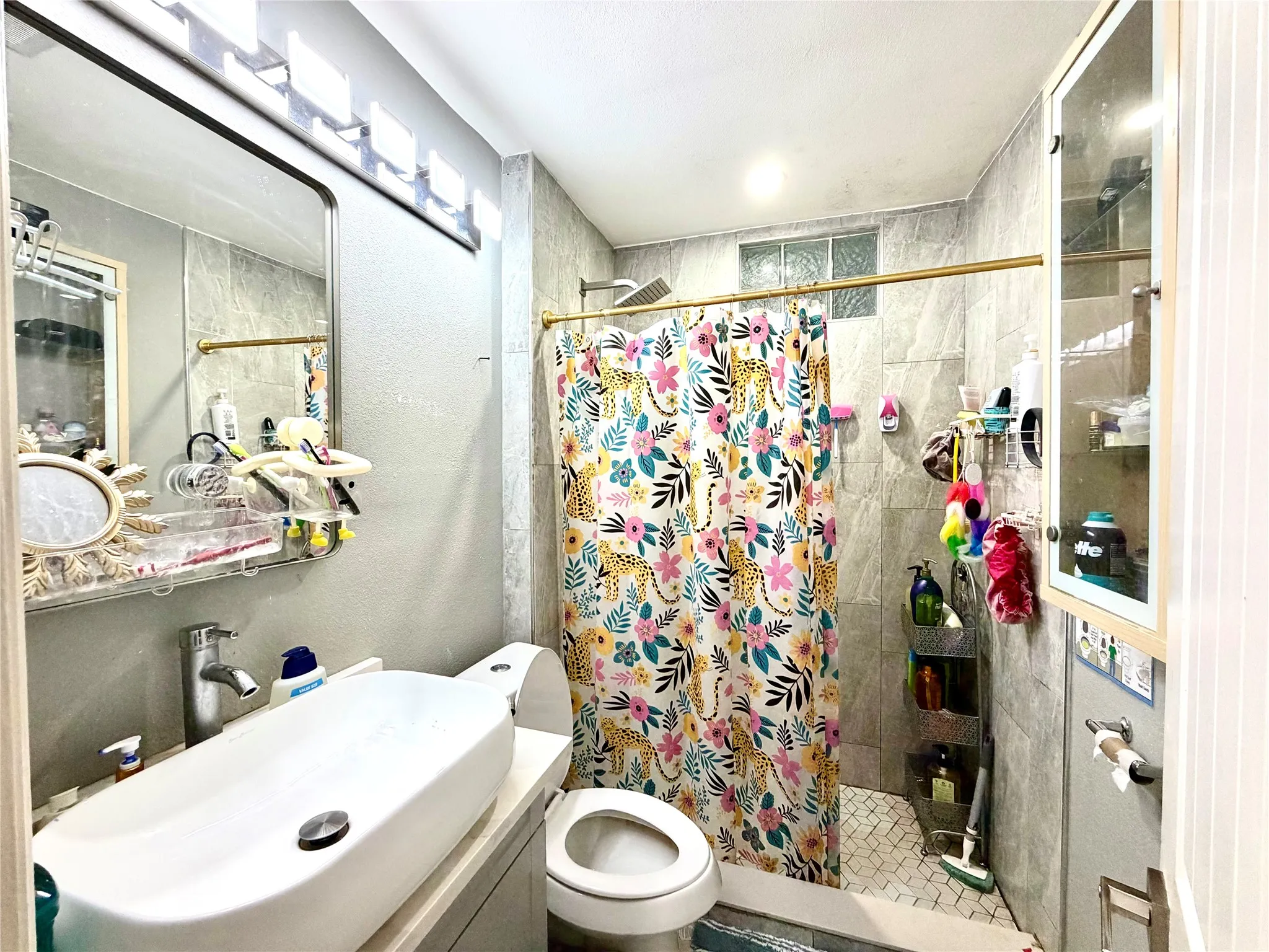 Bathroom featuring a vessel sink, full vanity mirror with task lighting, and a shower area with a gold-tone shower rod