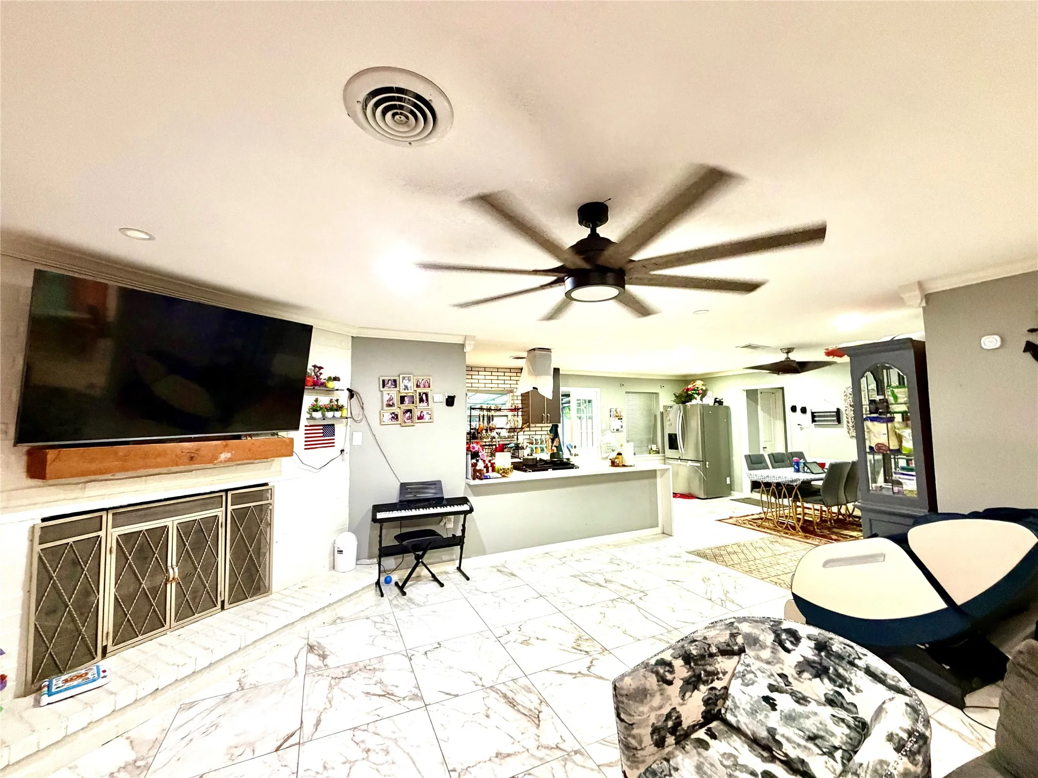 Open-concept living space featuring marble-look tile flooring, a fireplace with a white brick surround and wood mantle, and multiple ceiling fans