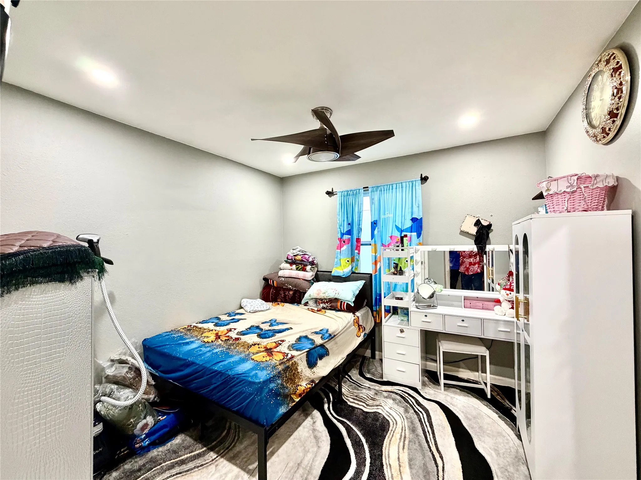 Recessed lighting illuminates this room featuring light gray walls, a ceiling fan with integrated lighting, and a window with a dark-finished curtain rod