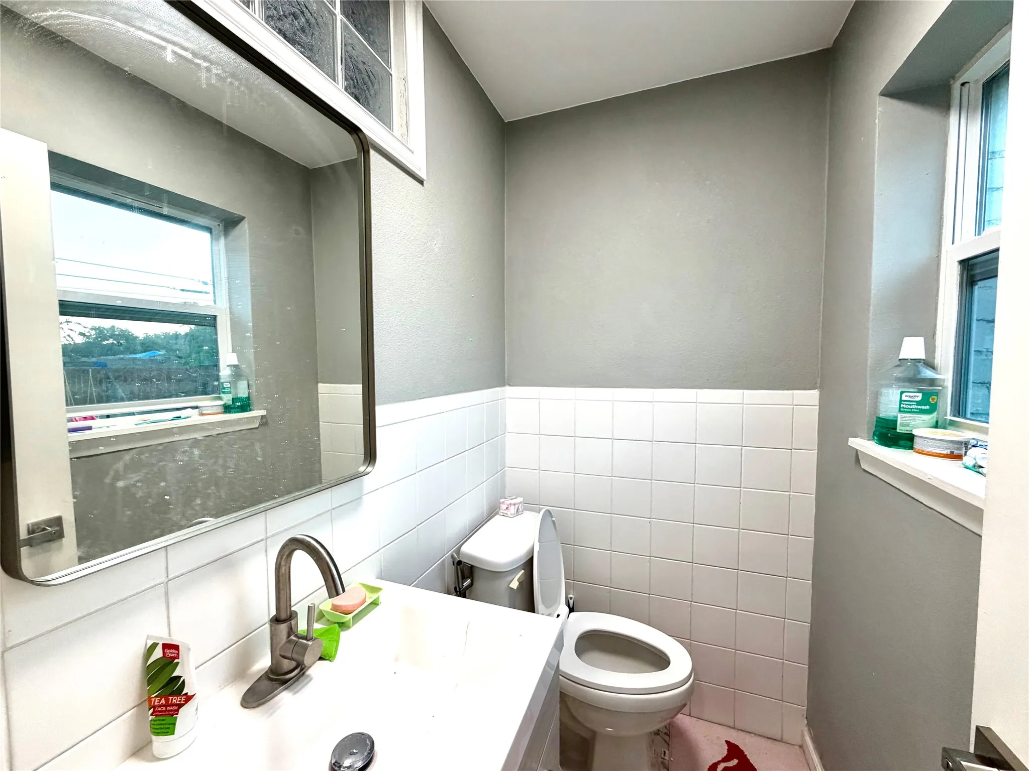 Bathroom featuring a wall-mounted mirror, single-handle faucet, white tile wainscoting, and a window with a sill