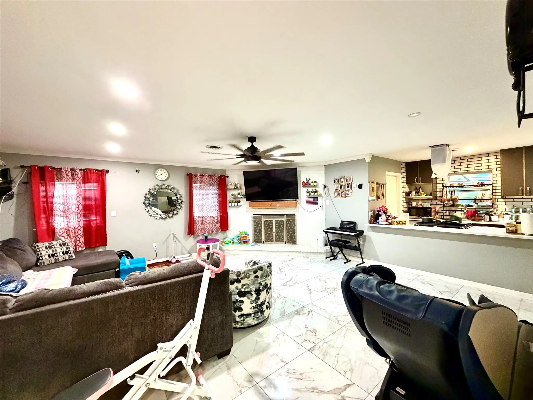 Spacious living area featuring polished tile flooring, recessed ceiling lighting, a ceiling fan, and a built-in fireplace with a stone surround
