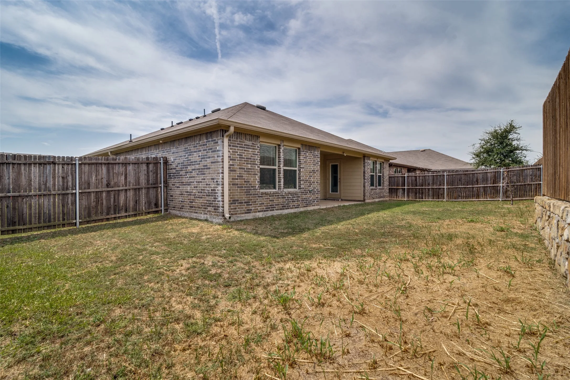 Brick exterior with a covered patio, multiple windows, and a wood privacy fence