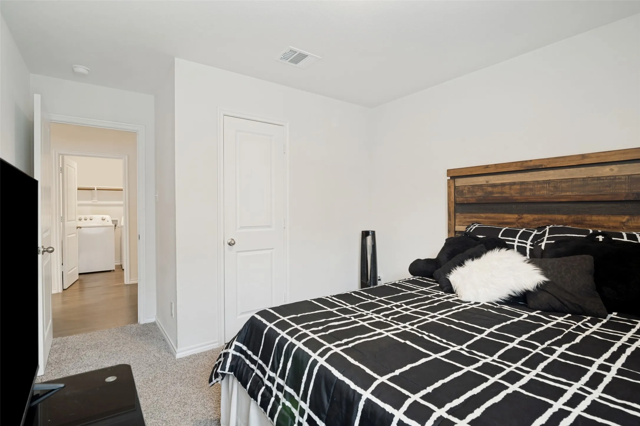 Carpeting, wood-finish headboard, laundry area with built-in shelving, white paneled doors, and white walls