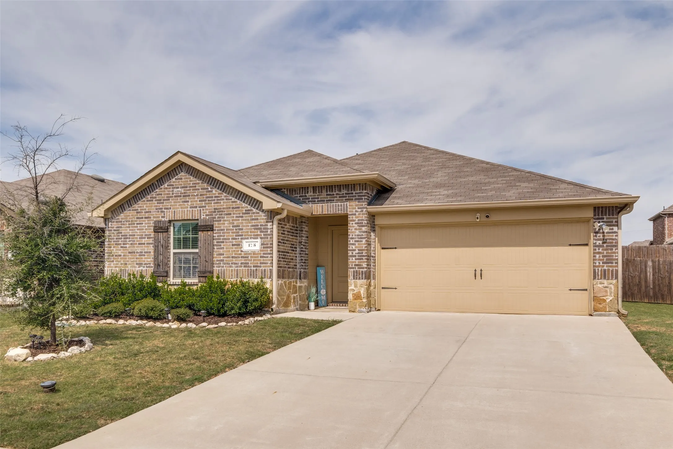 Brick and stone facade, attached two-car garage, mature landscaping, and an extended driveway