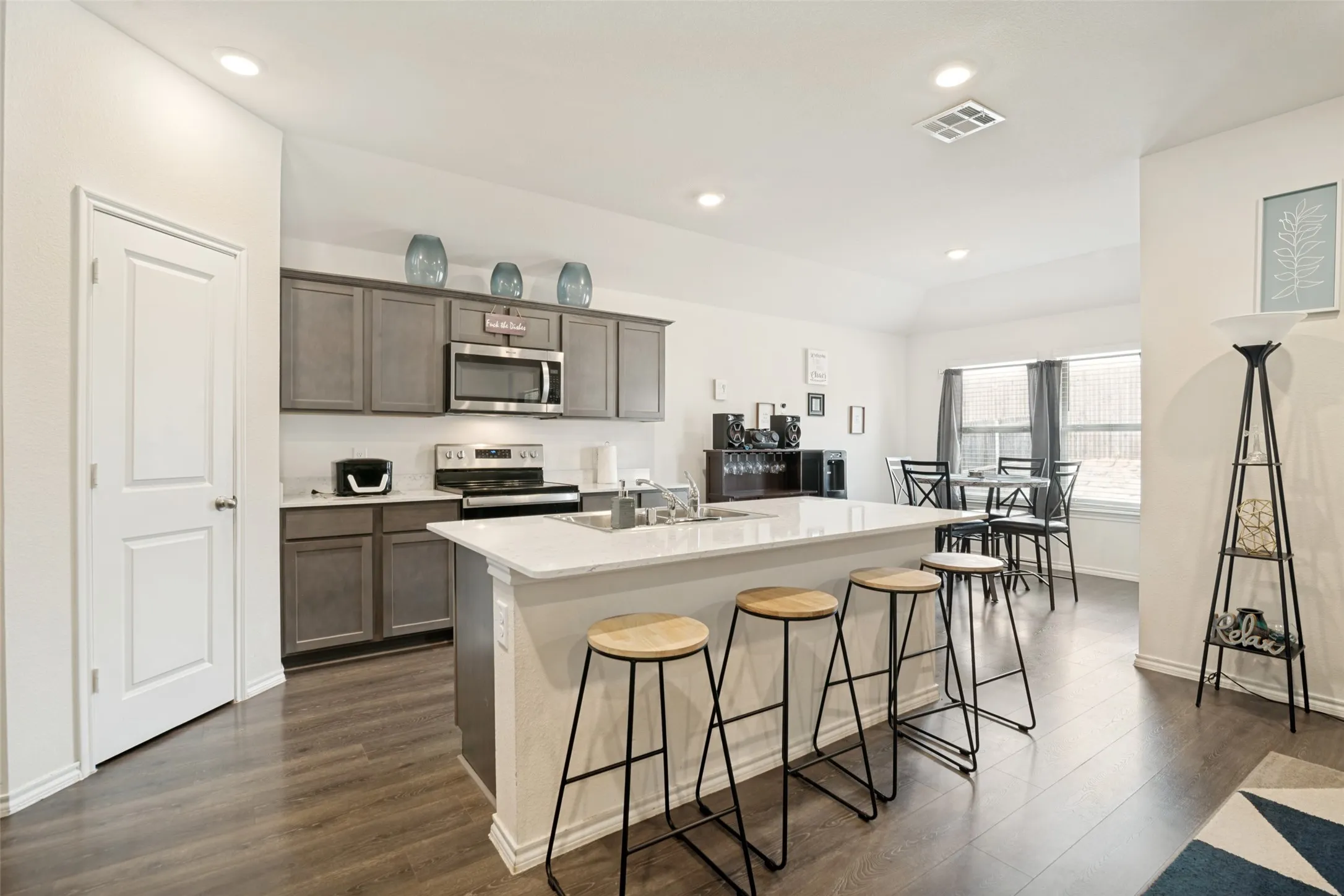 Kitchen featuring wood-finish flooring, an expansive island with countertop seating, gray cabinetry, stainless steel appliances, and recessed lighting