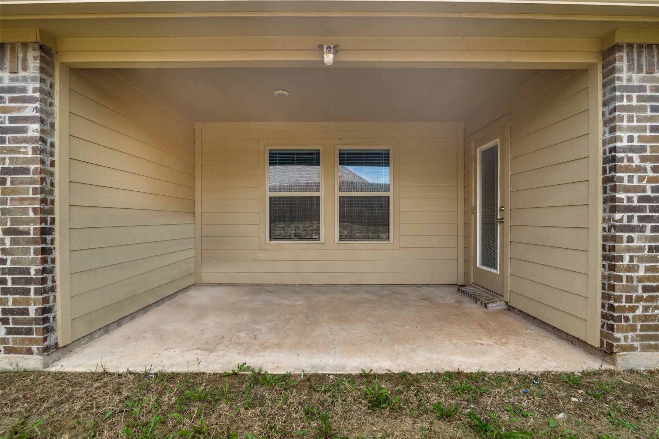 Covered patio featuring concrete flooring, tan siding, and brick accents