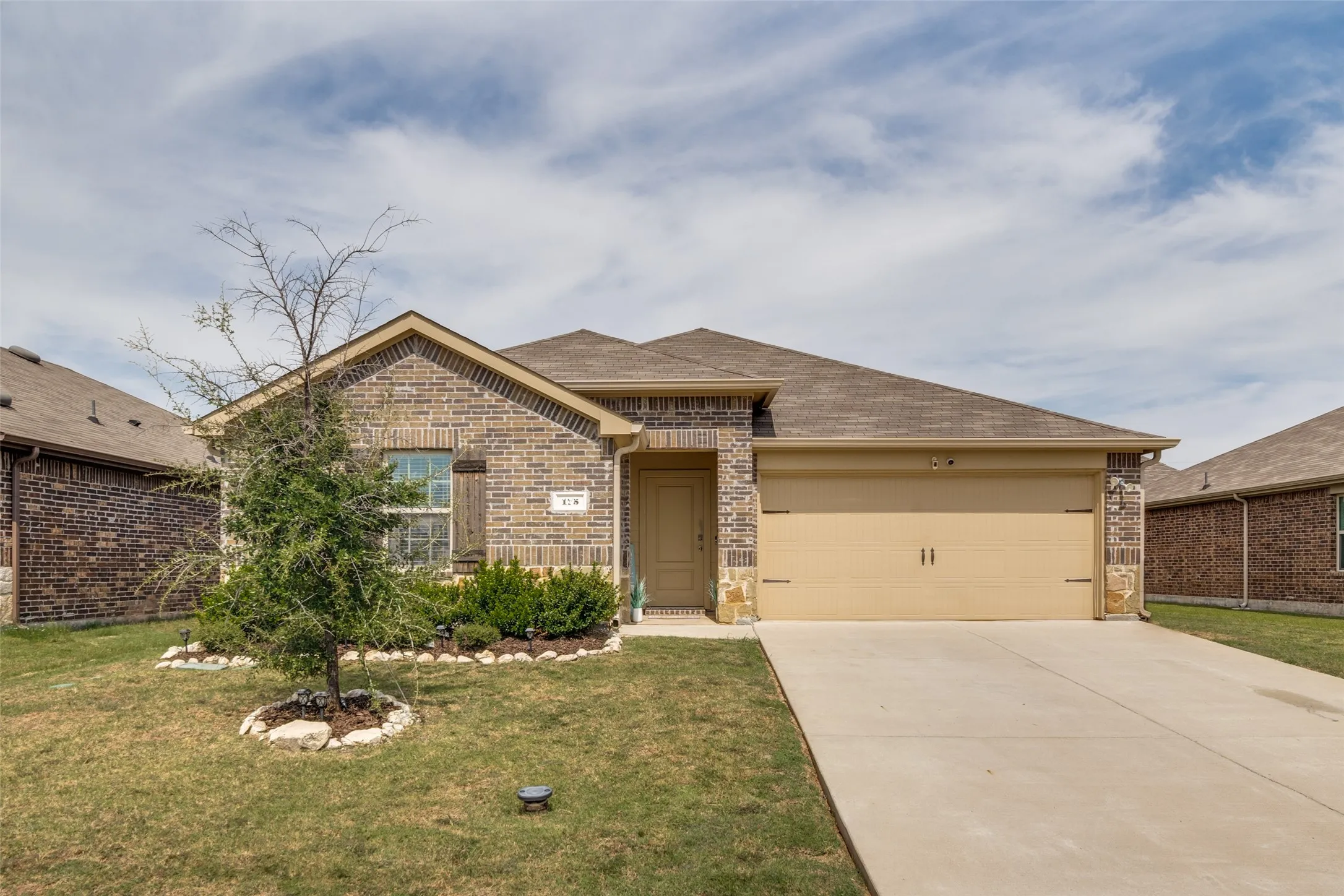 Brick and stone facade, attached garage, concrete driveway, and established landscaping
