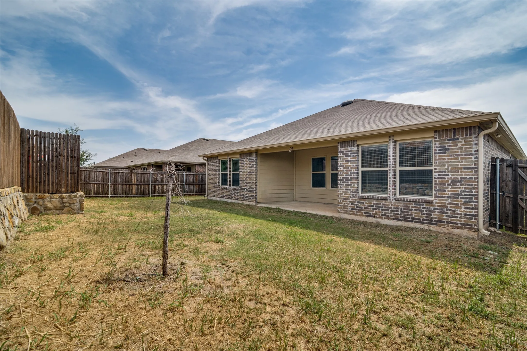 Brick exterior with multiple windows, covered patio, privacy fencing, and wood gate access