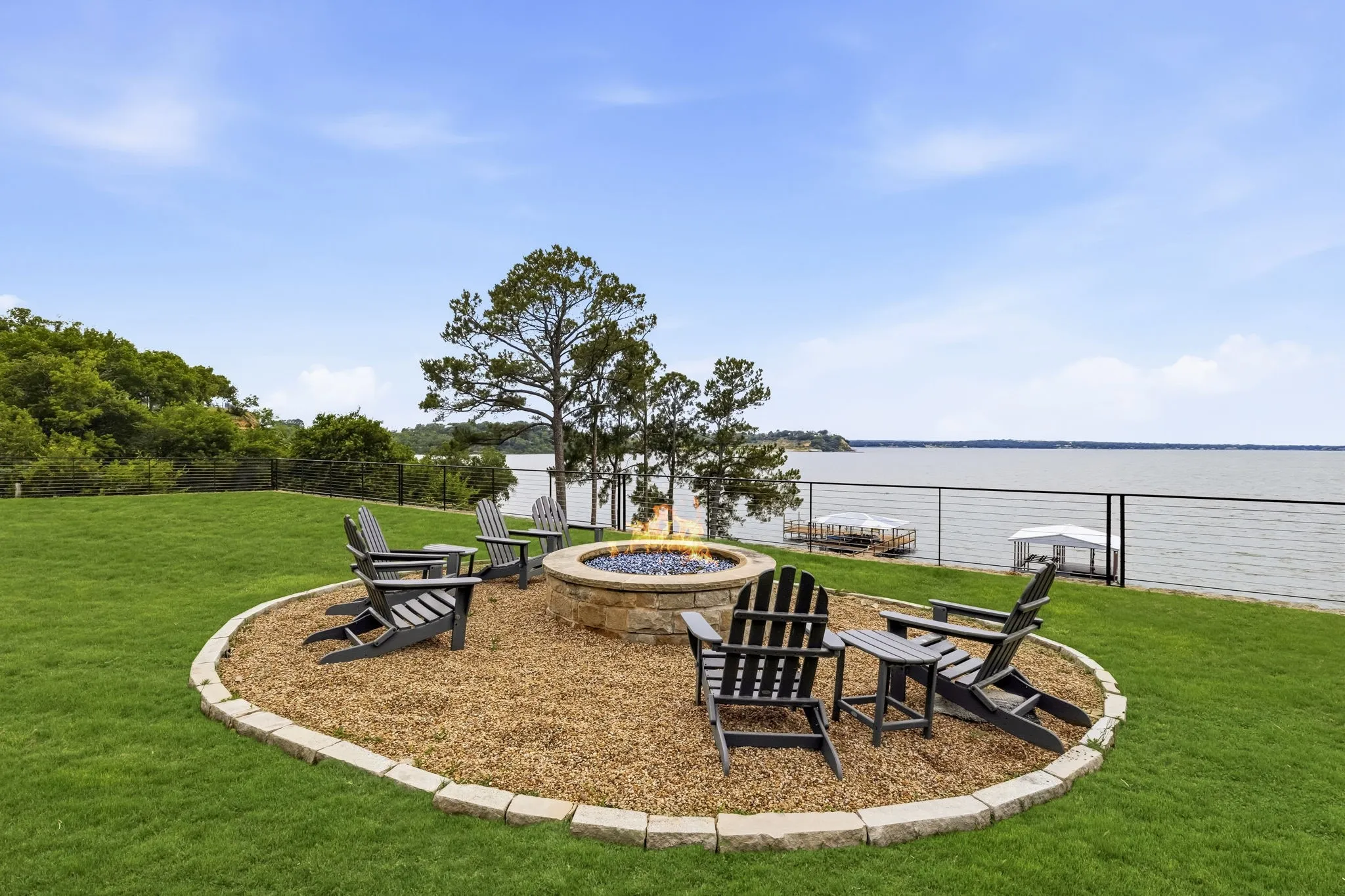 Manicured lawn with a stone-edged fire pit area, featuring a stone fire pit, and a lakefront setting