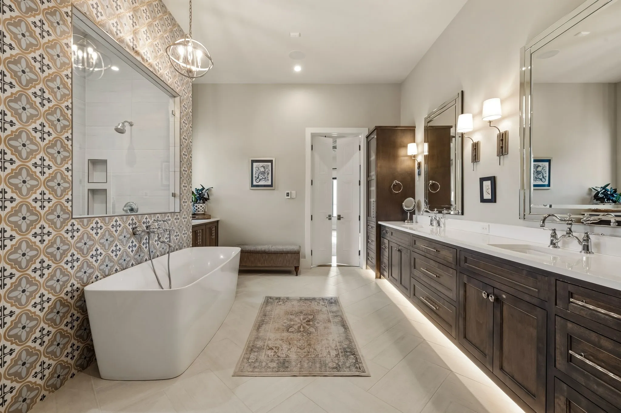 Spacious bathroom featuring a freestanding tub, glass-enclosed shower, dual vanities with quartz countertops, custom wood cabinetry, and large format floor tiling