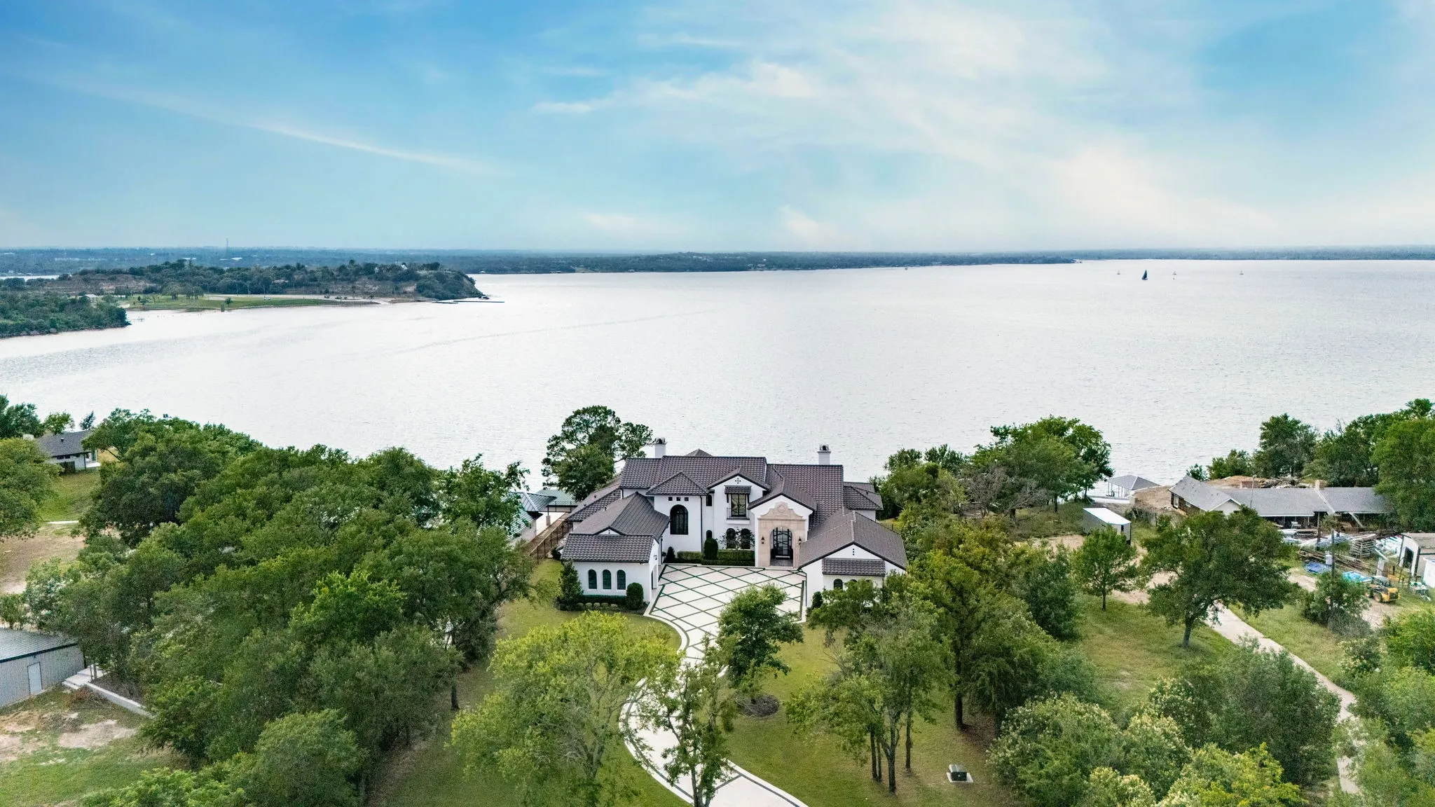 Waterfront property with a large white residence, dark shingle roof, and a patterned driveway