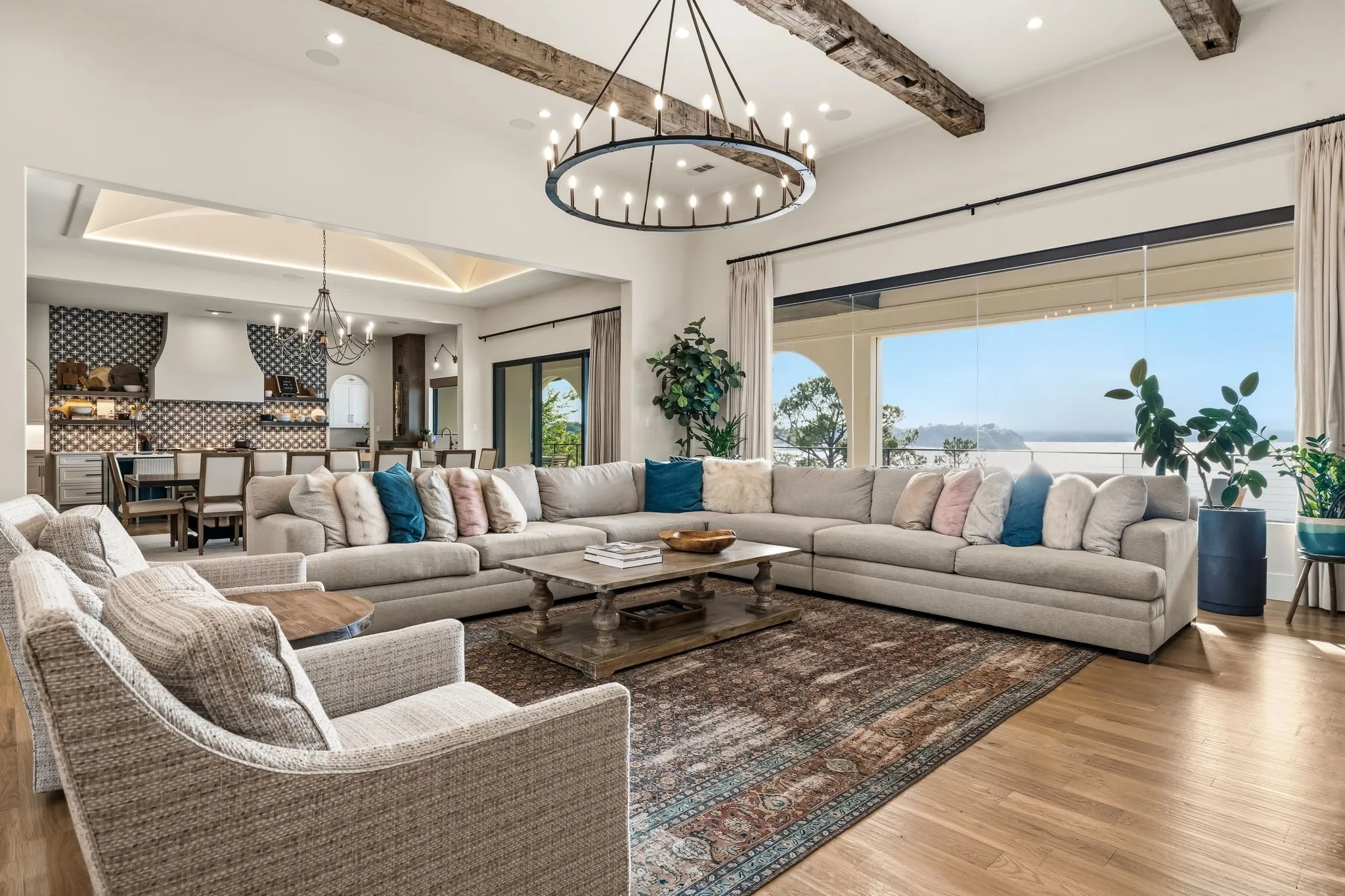 Vaulted ceiling with exposed wood beams, hardwood flooring, large picture window, open-concept living space, and a circular chandelier