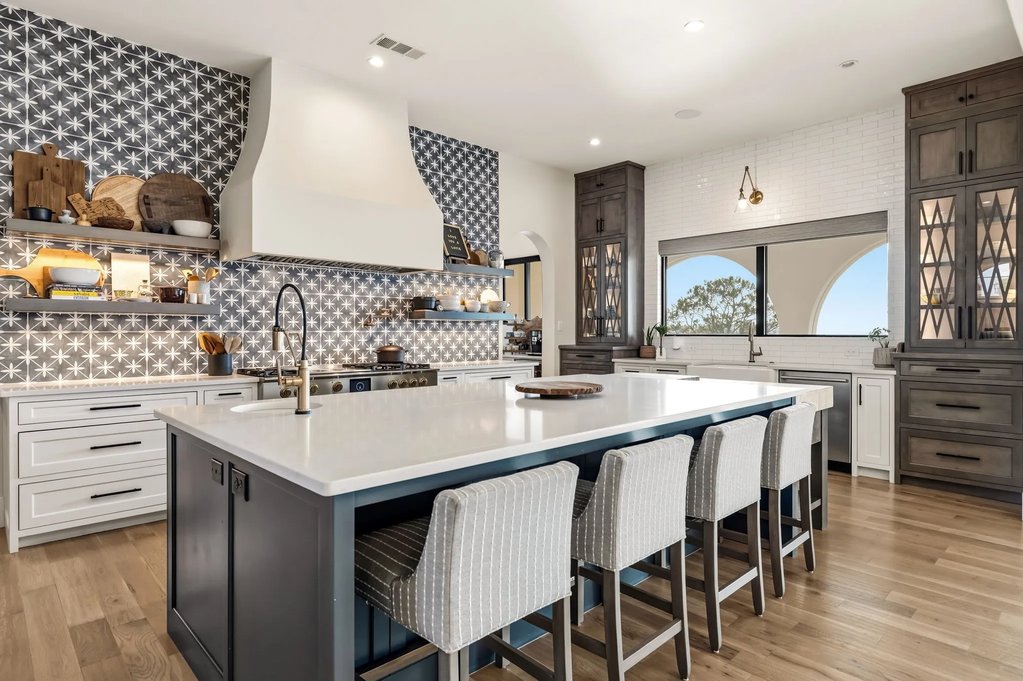 Expansive kitchen island with a light-toned countertop, wood-finish flooring, patterned tile backsplash, white subway tile accents, and integrated wooden cabinetry