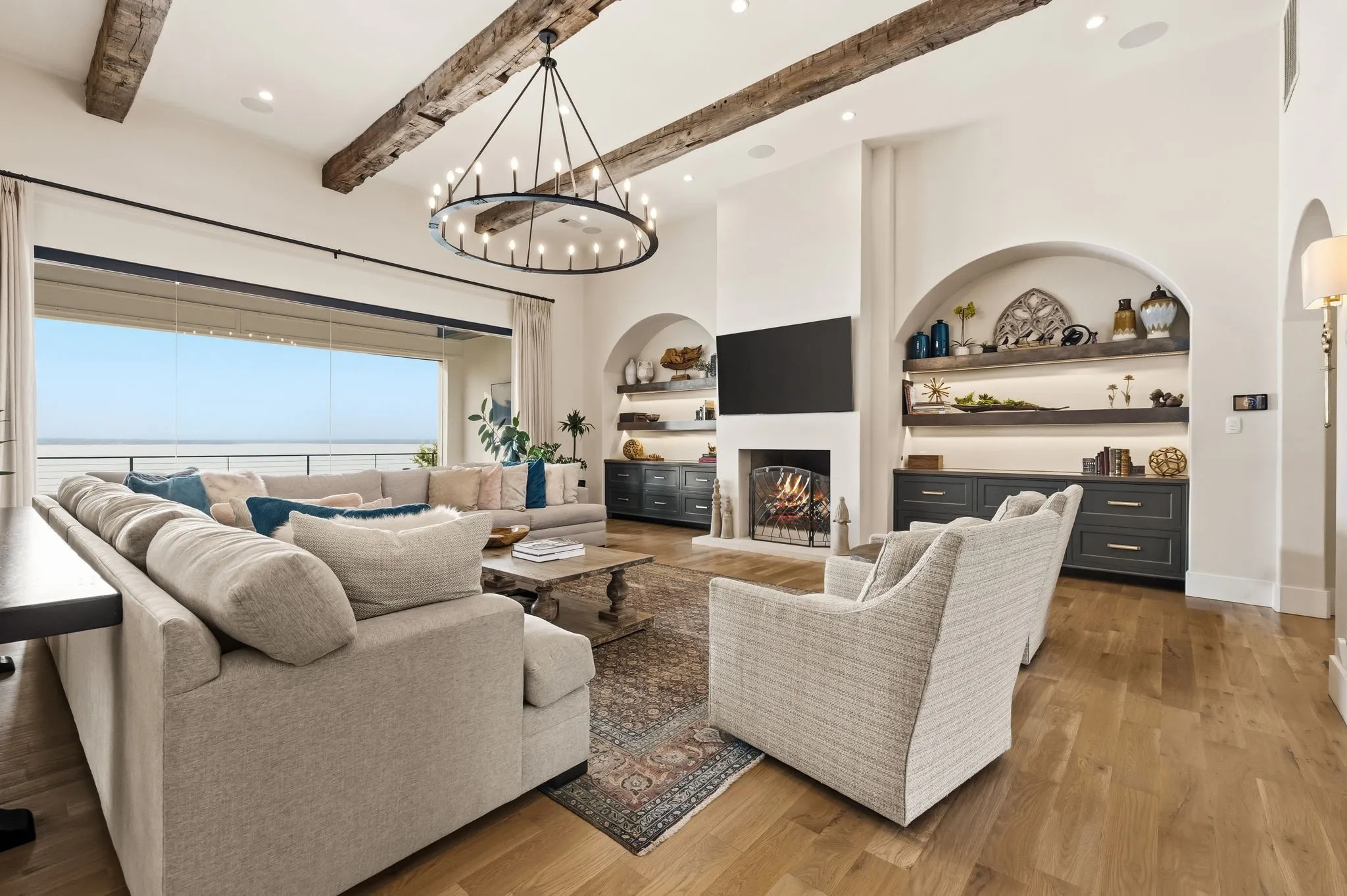 Wood-finish flooring, exposed ceiling beams, large chandelier, built-in shelving, and a fireplace