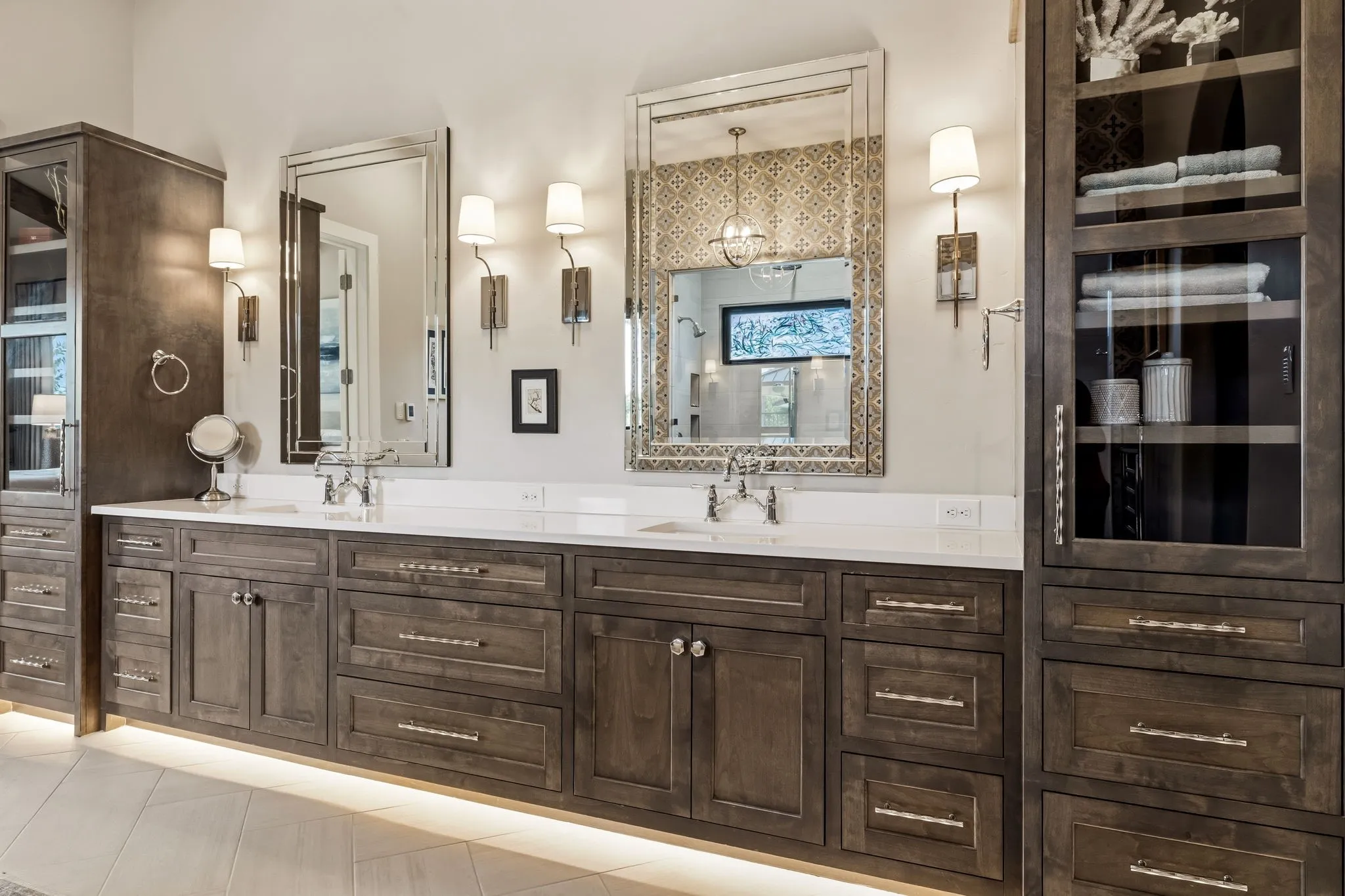 Dual vanity with integrated sinks, white countertops, dark wood-finish cabinetry, under-cabinet lighting, and wall-mounted mirrors