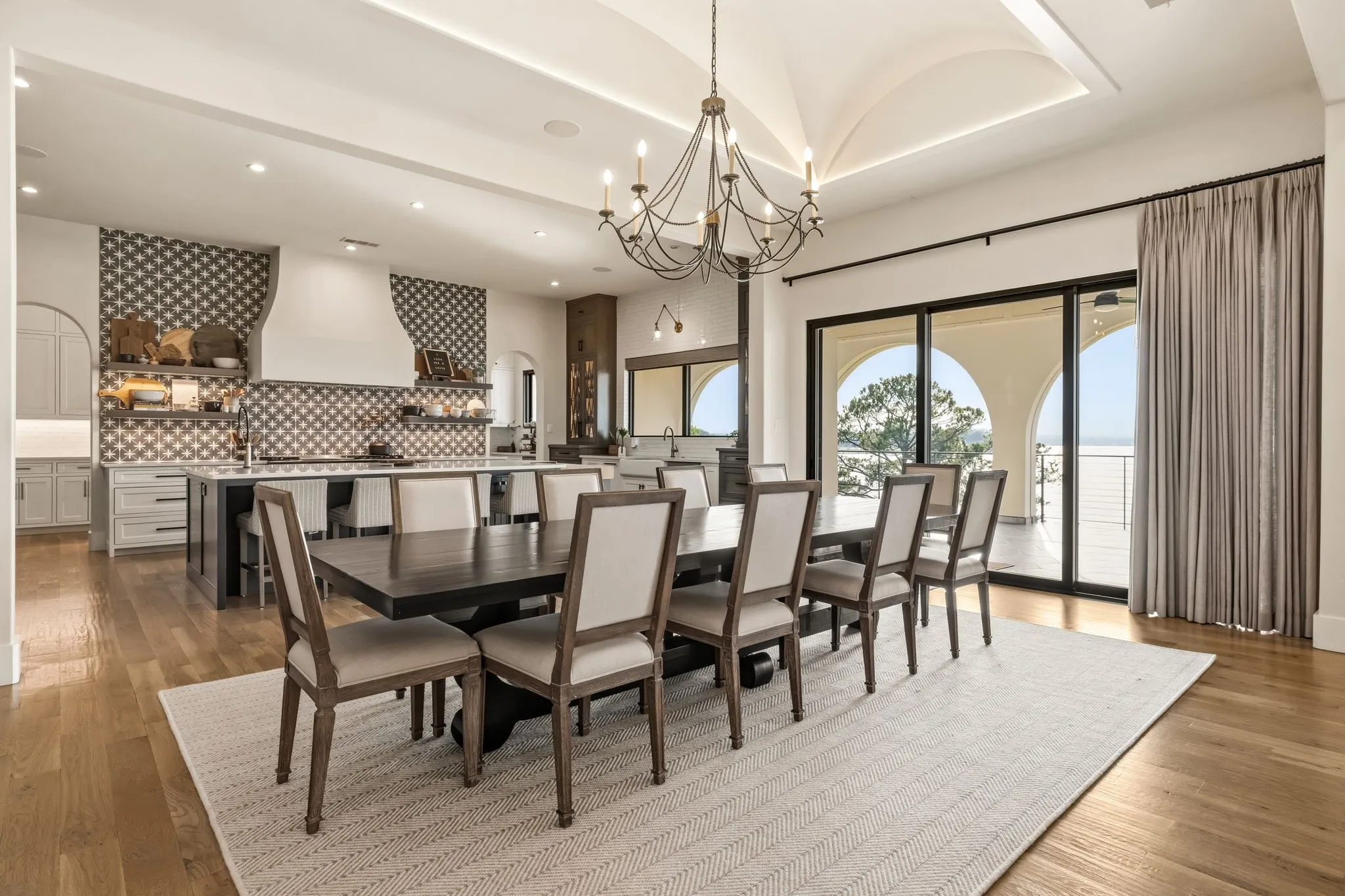 Open-concept living area featuring a vaulted ceiling with accent lighting, hardwood flooring, and a large sliding glass door with arched patio access