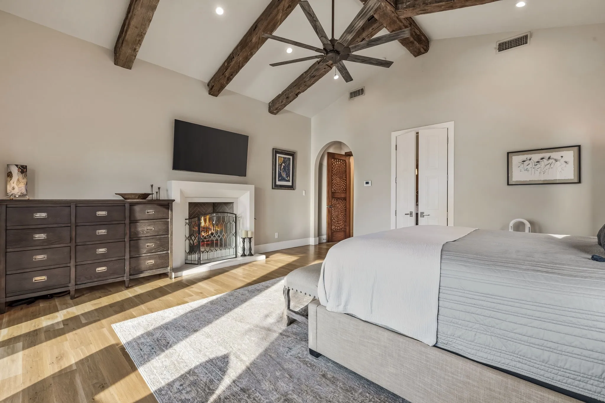 Vaulted ceiling with exposed wood beams, wood-finish flooring, recessed lighting, and a stone-surround fireplace