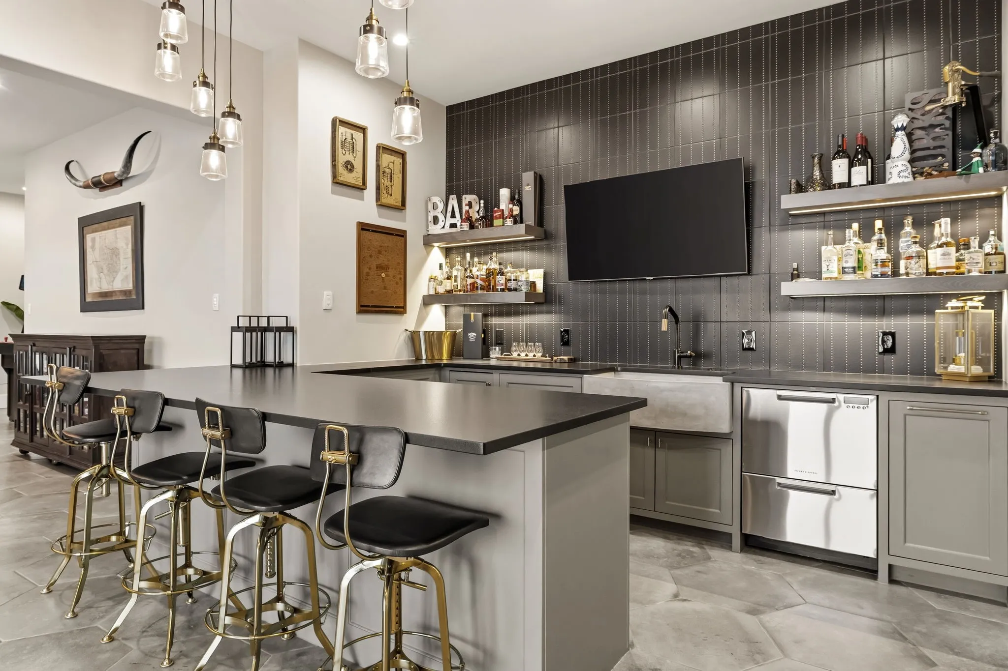 Custom bar area featuring a large counter, built-in shelving with integrated lighting, a concrete farmhouse-style sink, and stainless steel refrigeration drawers